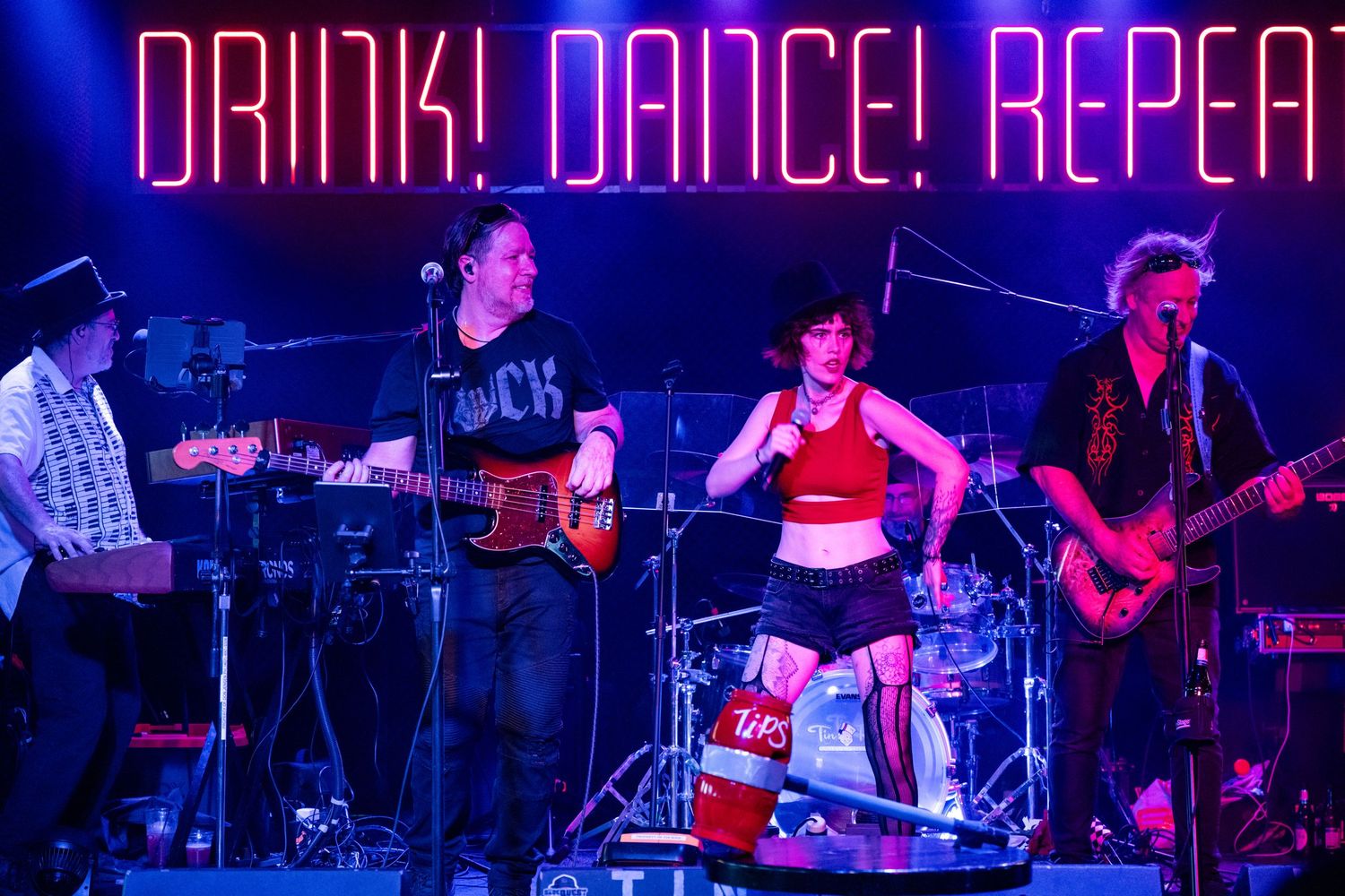 Neon sign reading 'DRINK! DANCE! REPEAT!' illuminated in blue and pink against dark background.
