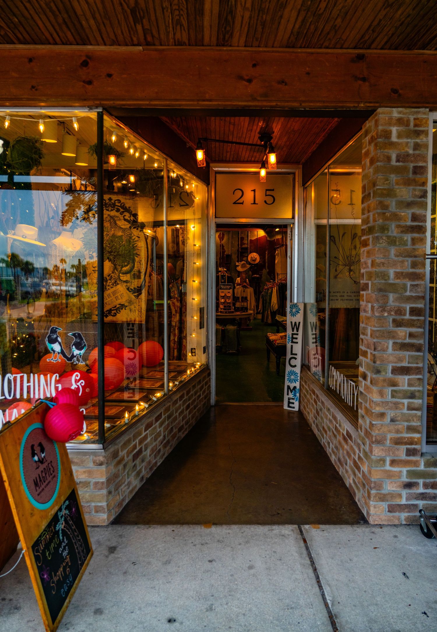 Illuminated storefront entrance with brick walls, display windows and string lights at dusk.