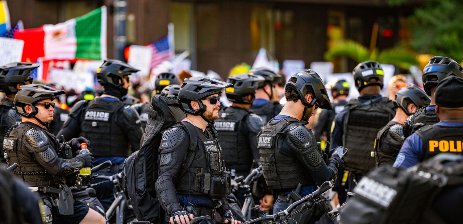 Police officers in tactical gear with bicycles form a line during a protest.
