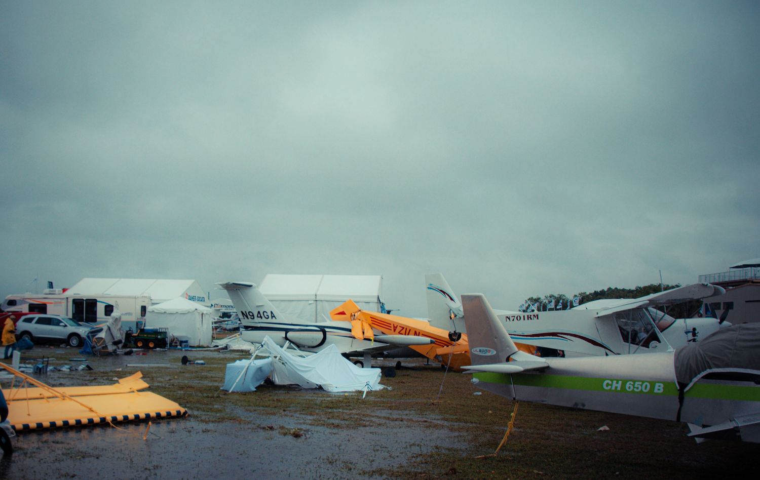 Storm clouds gather over a rural airfield with small planes and hangars visible in the panoramic view.