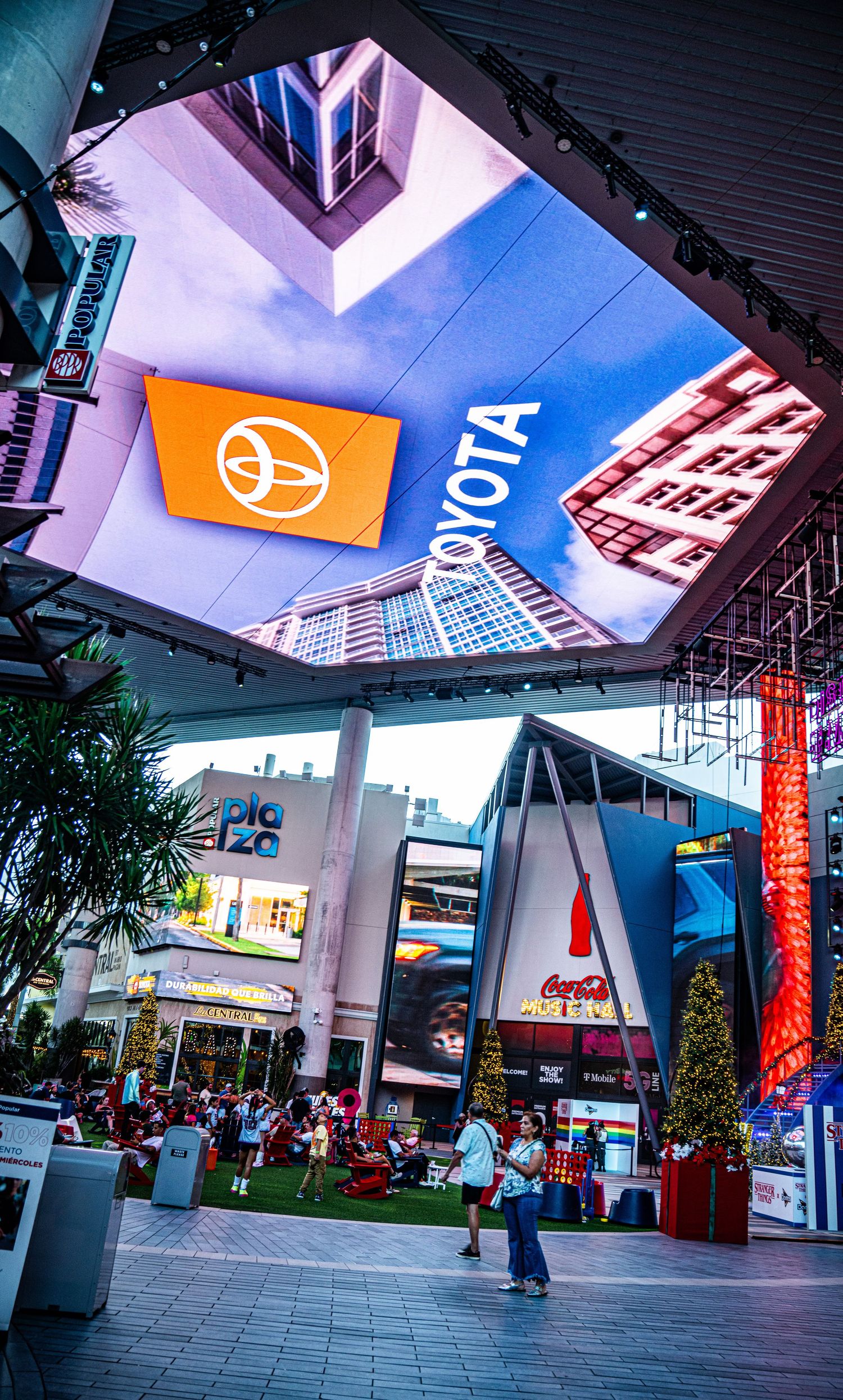 Modern urban plaza with Toyota signage and digital displays under dramatic blue and pink lighting at an outdoor shopping center.