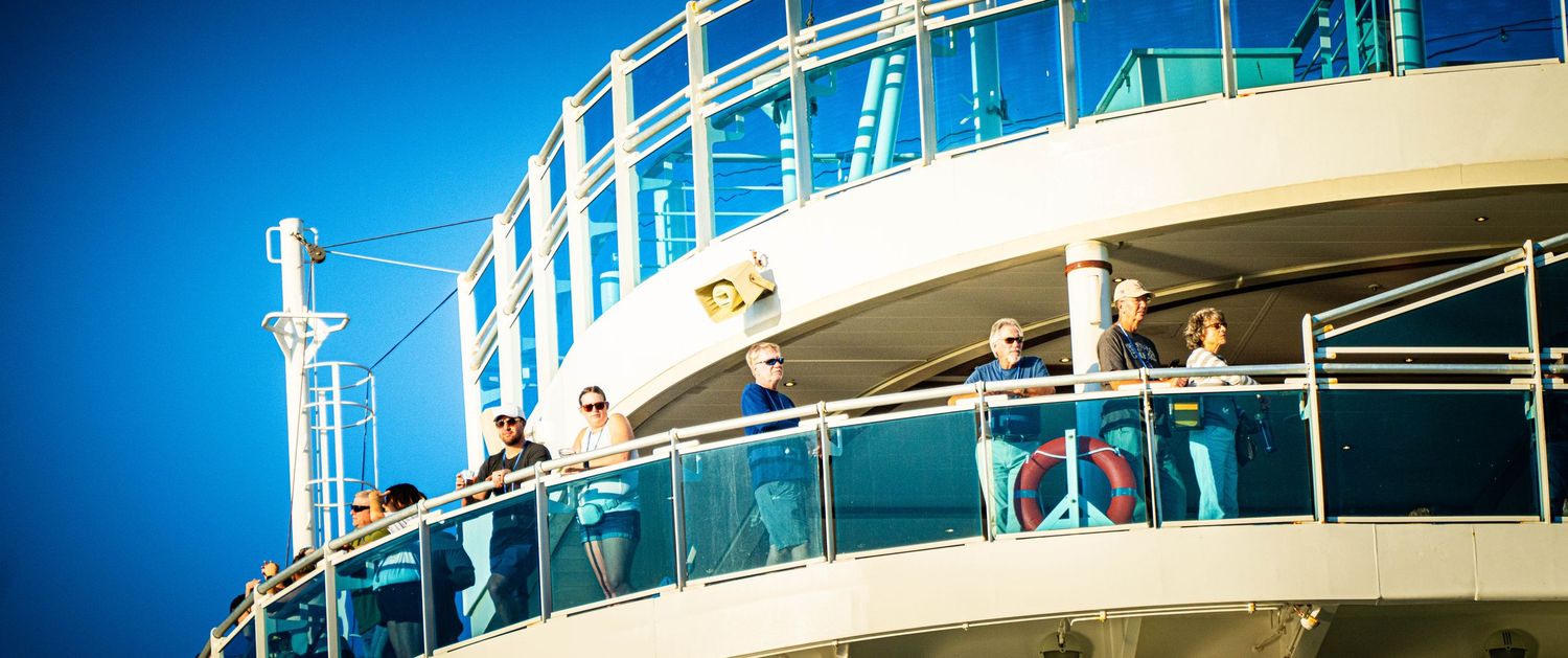 Cruise ship deck railing and balconies against a bright blue sky on a sunny day at sea.