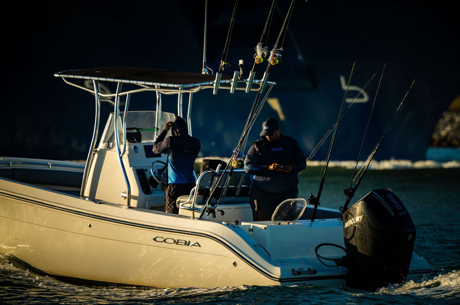 A series of boats moored at a marina during dusk with blue water and evening lighting visible.