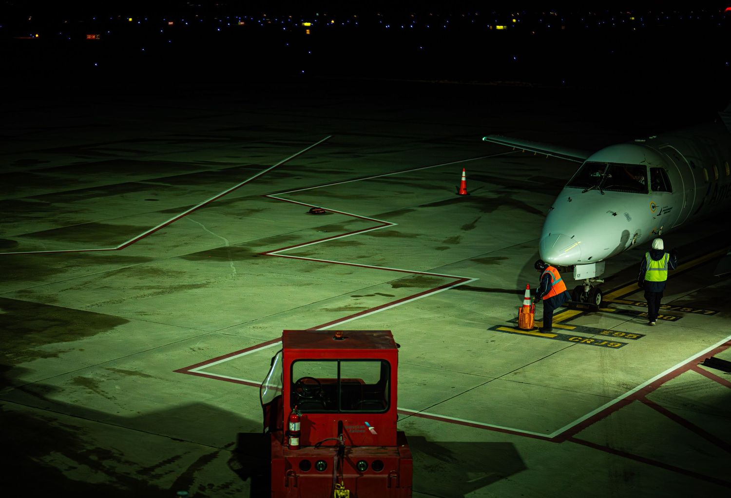 Aircraft and ground vehicles illuminated at night on an airport tarmac with green lighting visible.