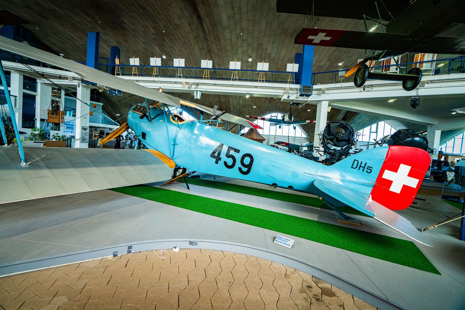 Vintage light blue DH-5 biplane numbered 459 with a Swiss cross on its tail, displayed in an aviation museum hall.