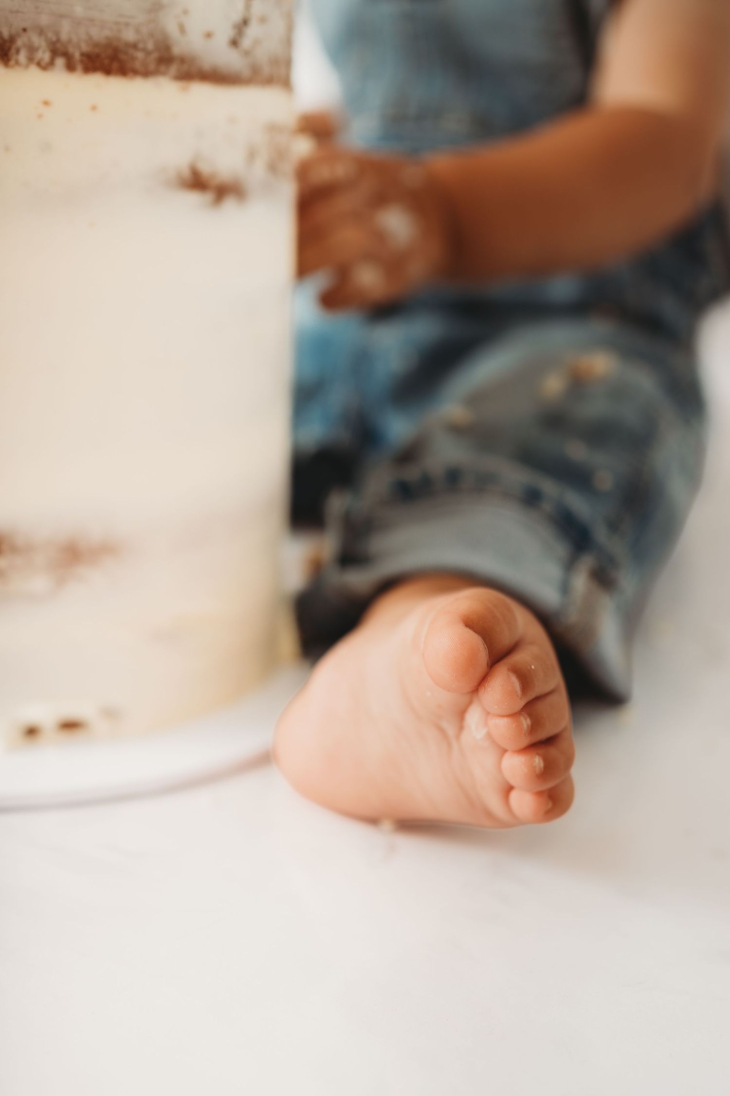 Close-up of a baby's bare foot beside a white cake during a first birthday cake smash photo session.