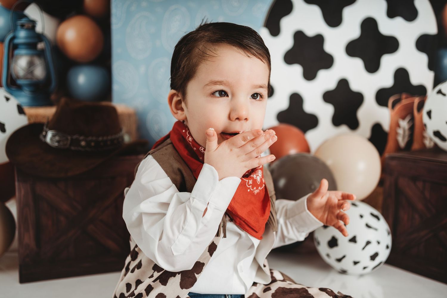 Adorable toddler in cowboy outfit with red bandana at a Western-themed first birthday cake smash photo session.