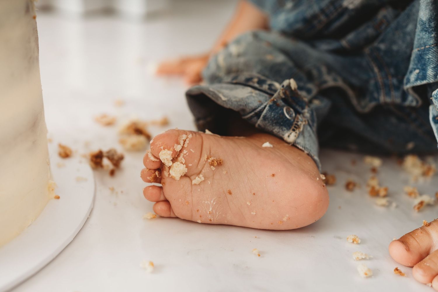 Close-up of a baby's foot covered in cake crumbs on a white floor during a first birthday smash cake celebration.