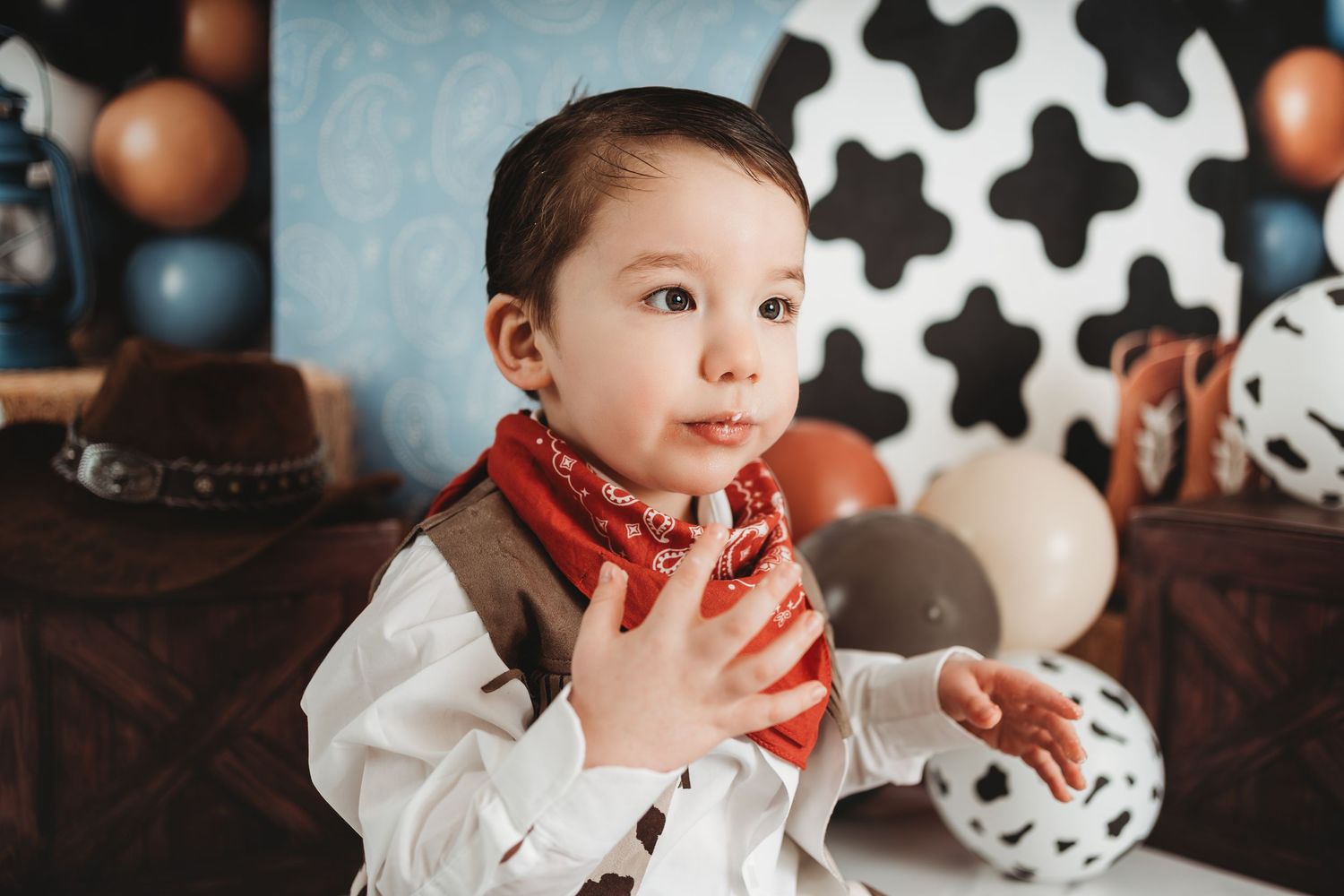 Adorable toddler boy in cowboy bandana and vest poses at a Western-themed first birthday party.