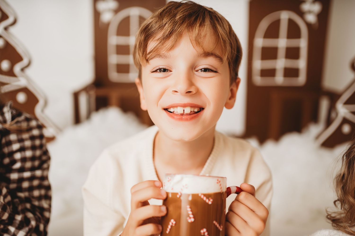 Smiling boy holding a festive gingerbread mug with marshmallows, surrounded by holiday decorations.