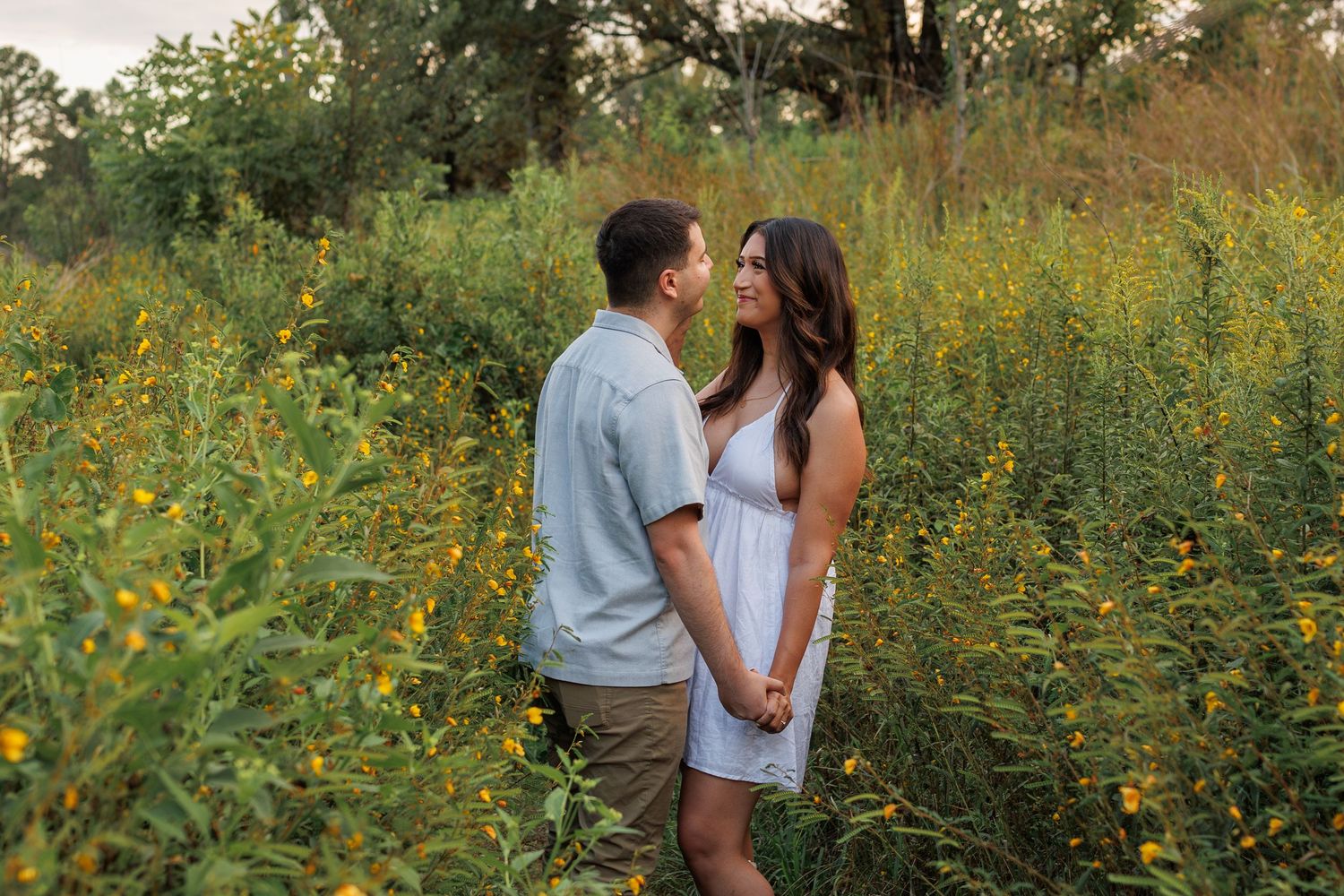 A couple embraces in a field of yellow wildflowers during a romantic outdoor photoshoot.