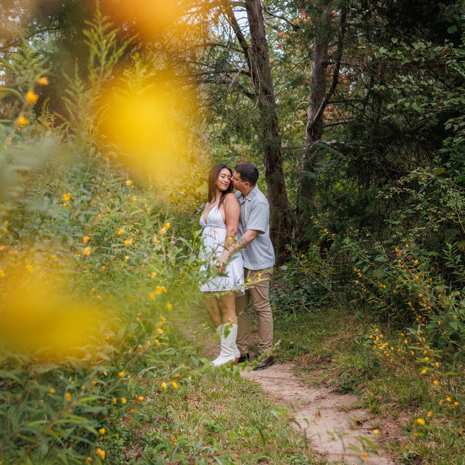 Couple sitting together on stone steps surrounded by yellow flowers and greenery in a garden setting.