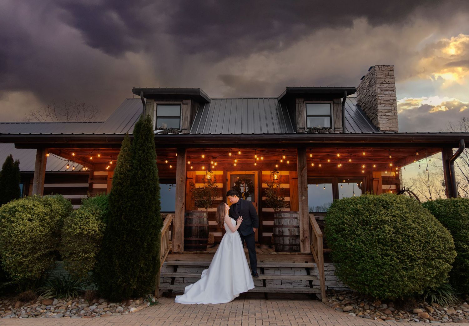 A dramatic storm sky frames a rustic wedding venue with twinkling lights and modern farmhouse design.