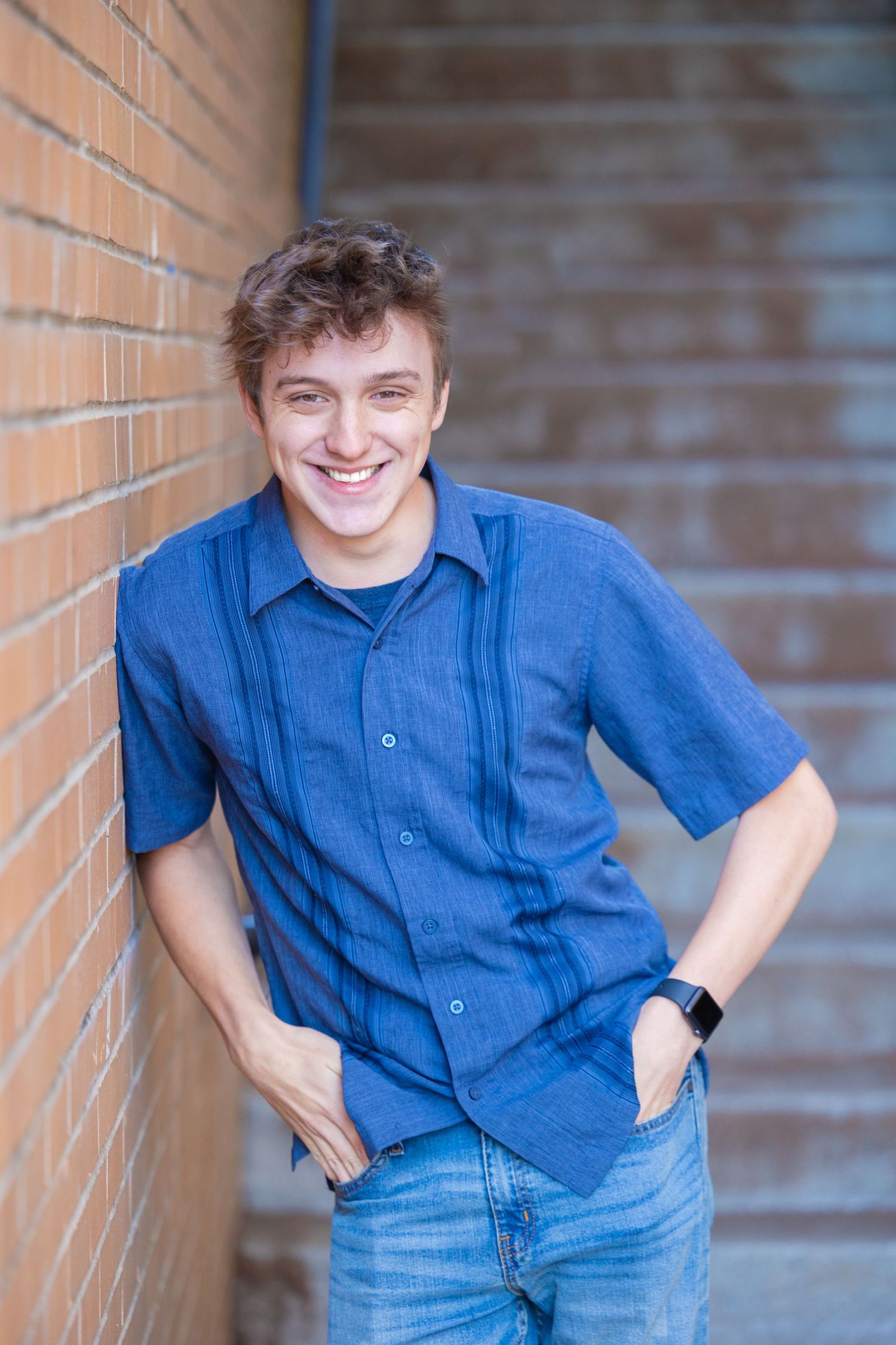 A casual portrait against a brick wall background in natural lighting.