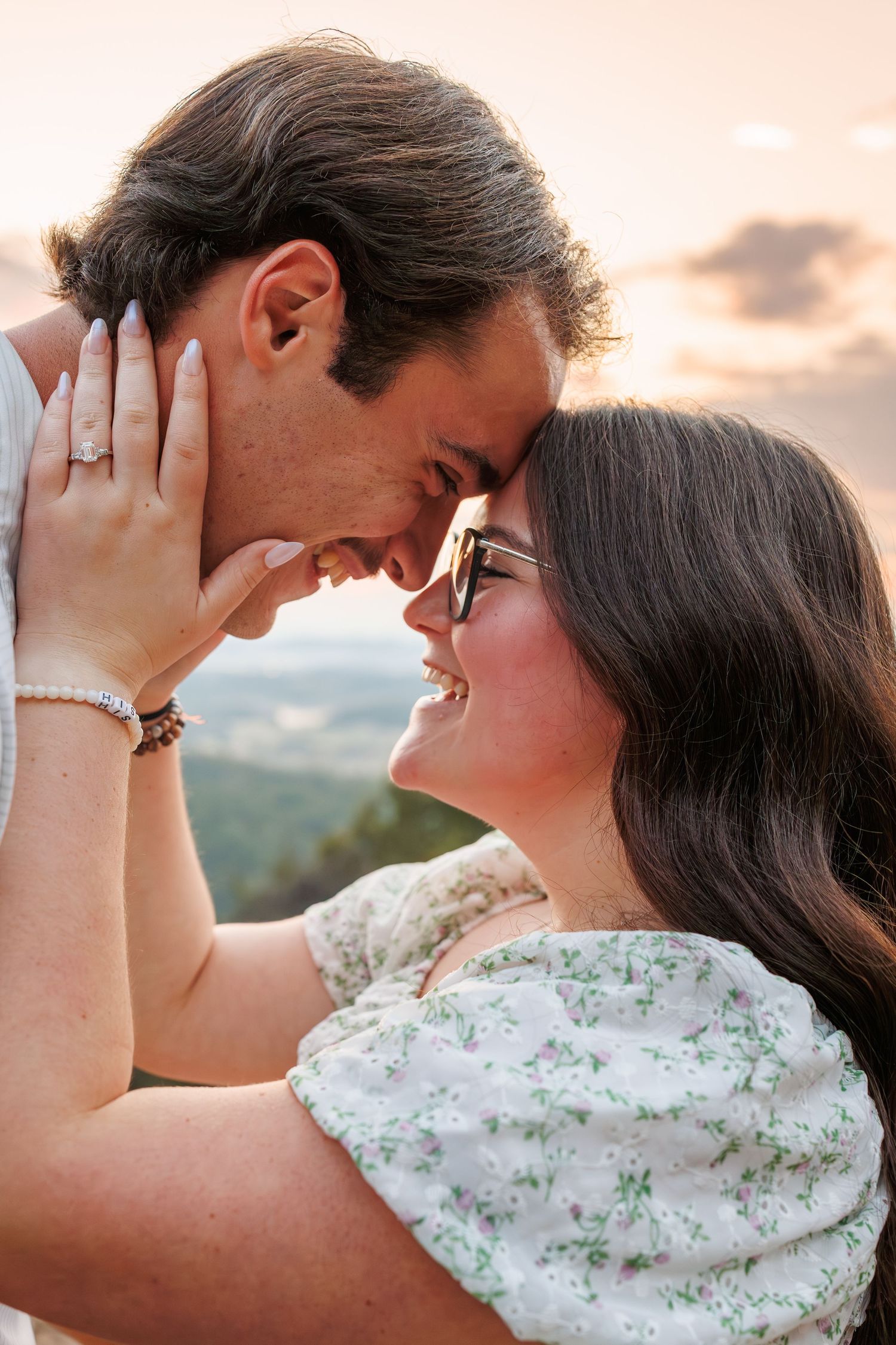 A romantic couple shares an intimate moment at sunset, with the woman wearing a floral dress against a warm sky backdrop.