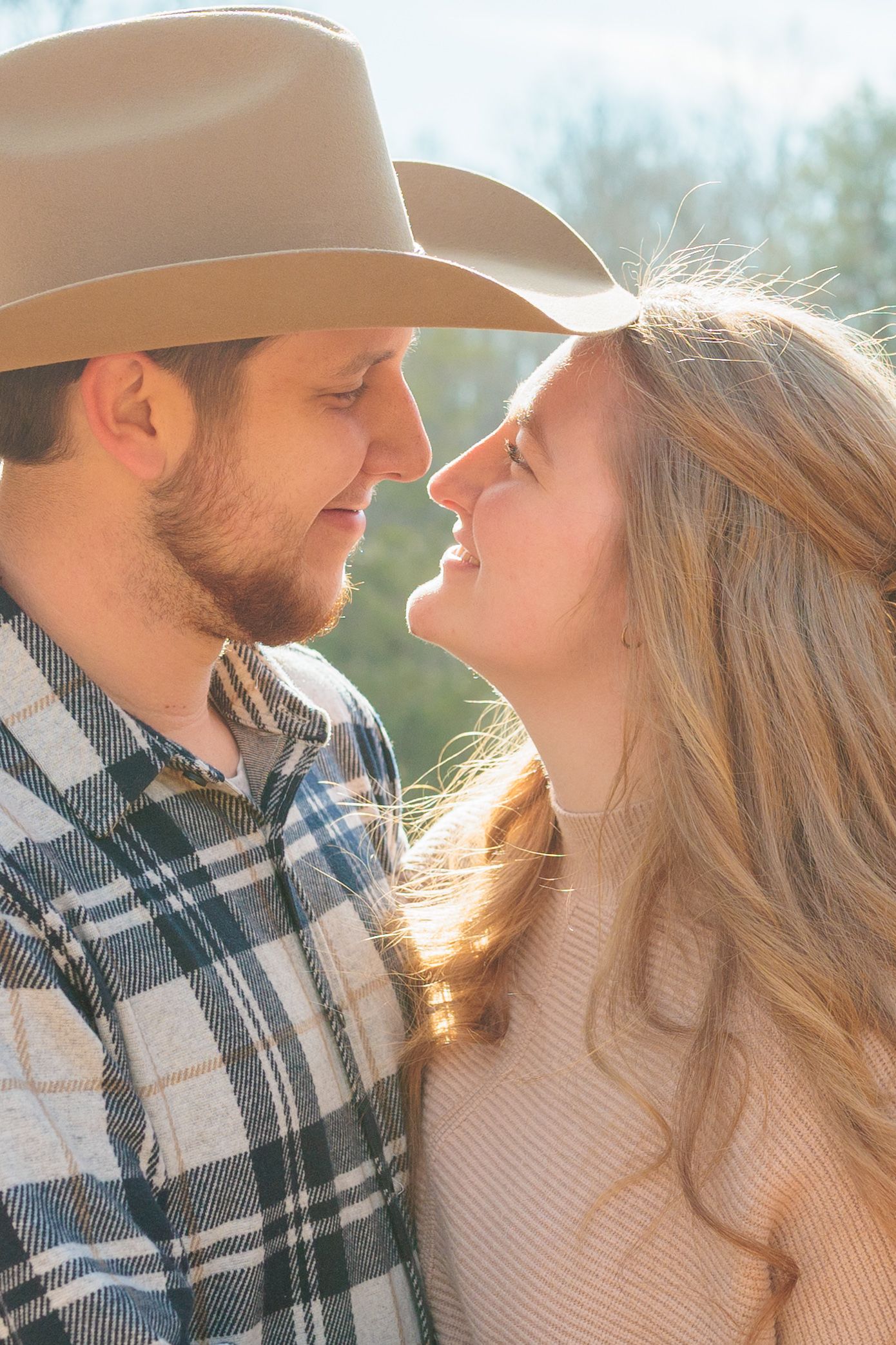 A romantic couple in plaid and beige sweater share an intimate moment outdoors in golden sunlight.