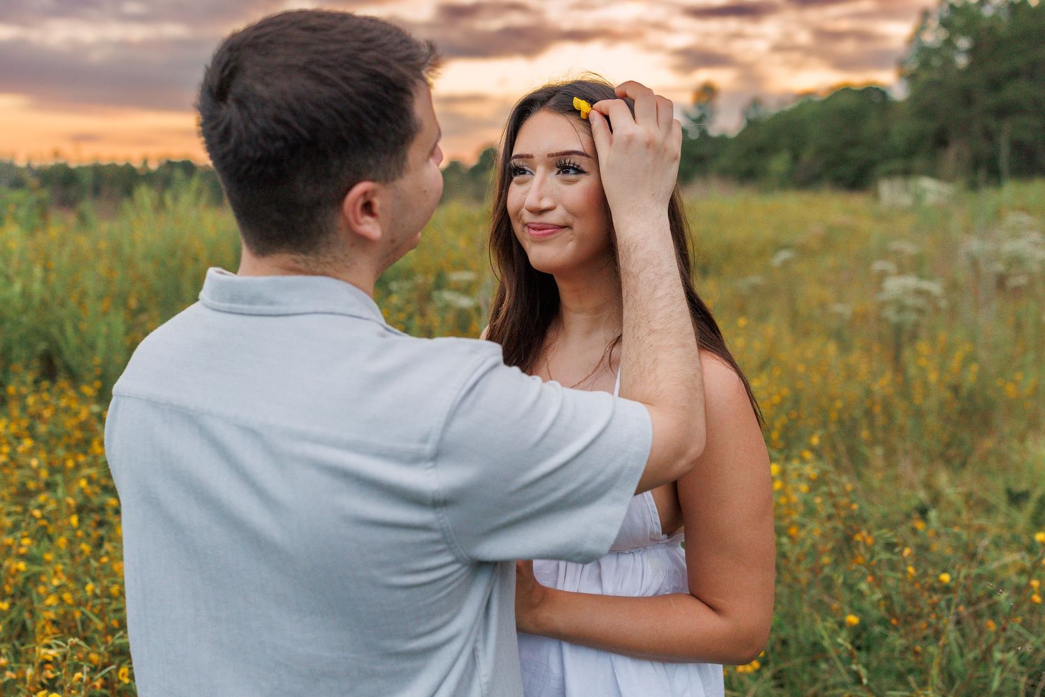 A couple shares an intimate moment against a vibrant sunset sky in a meadow of summer flowers.