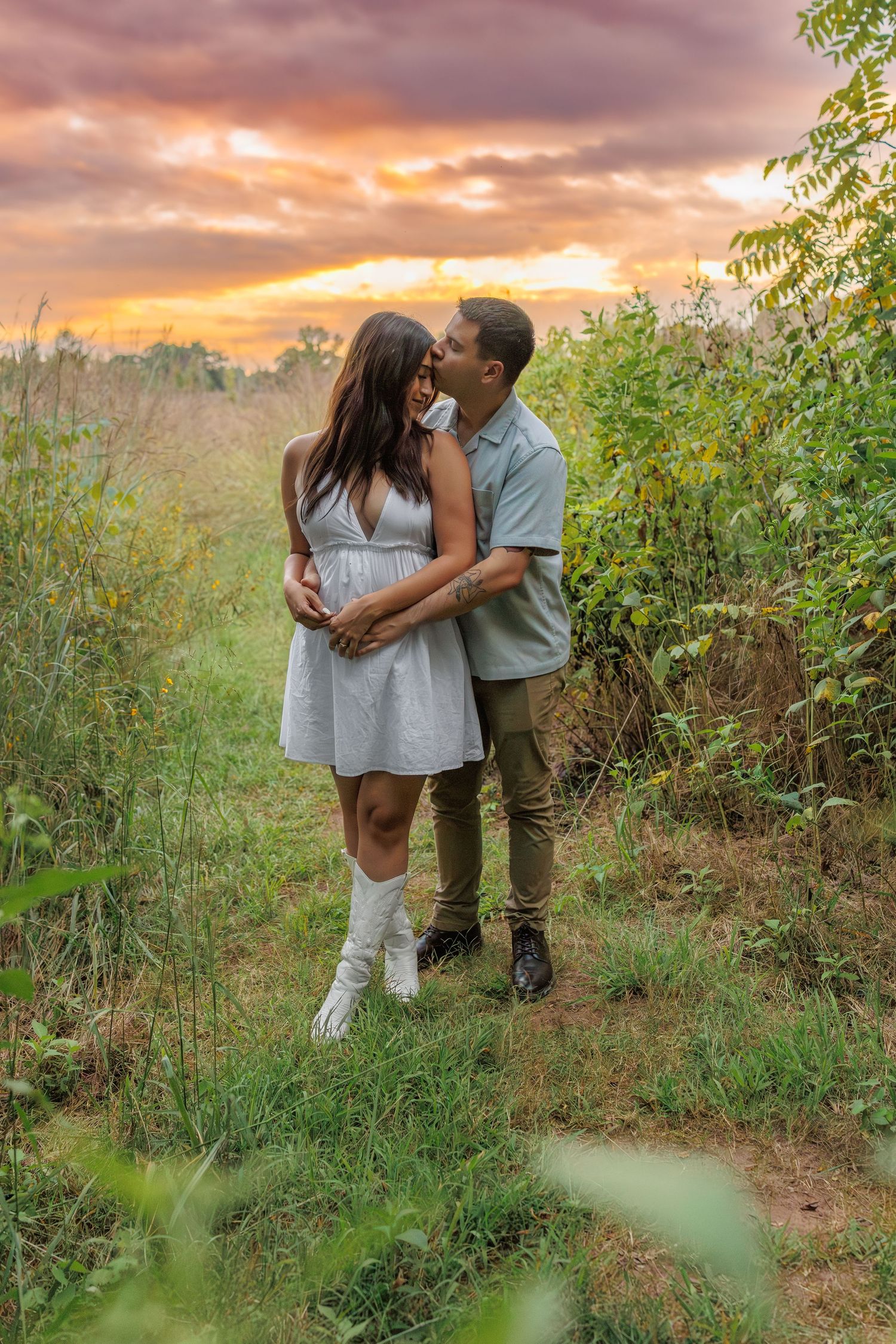 A romantic couple embraces in a scenic outdoor setting during a dramatic golden sunset.