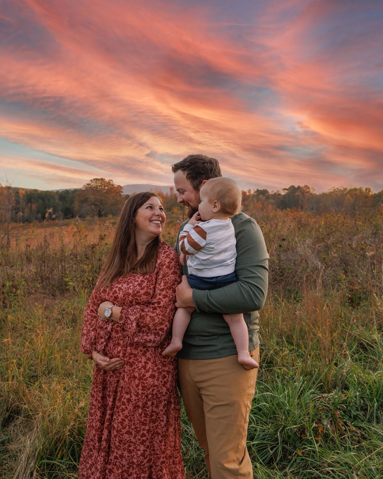 A family shares a tender moment in a golden autumn field during sunset.
