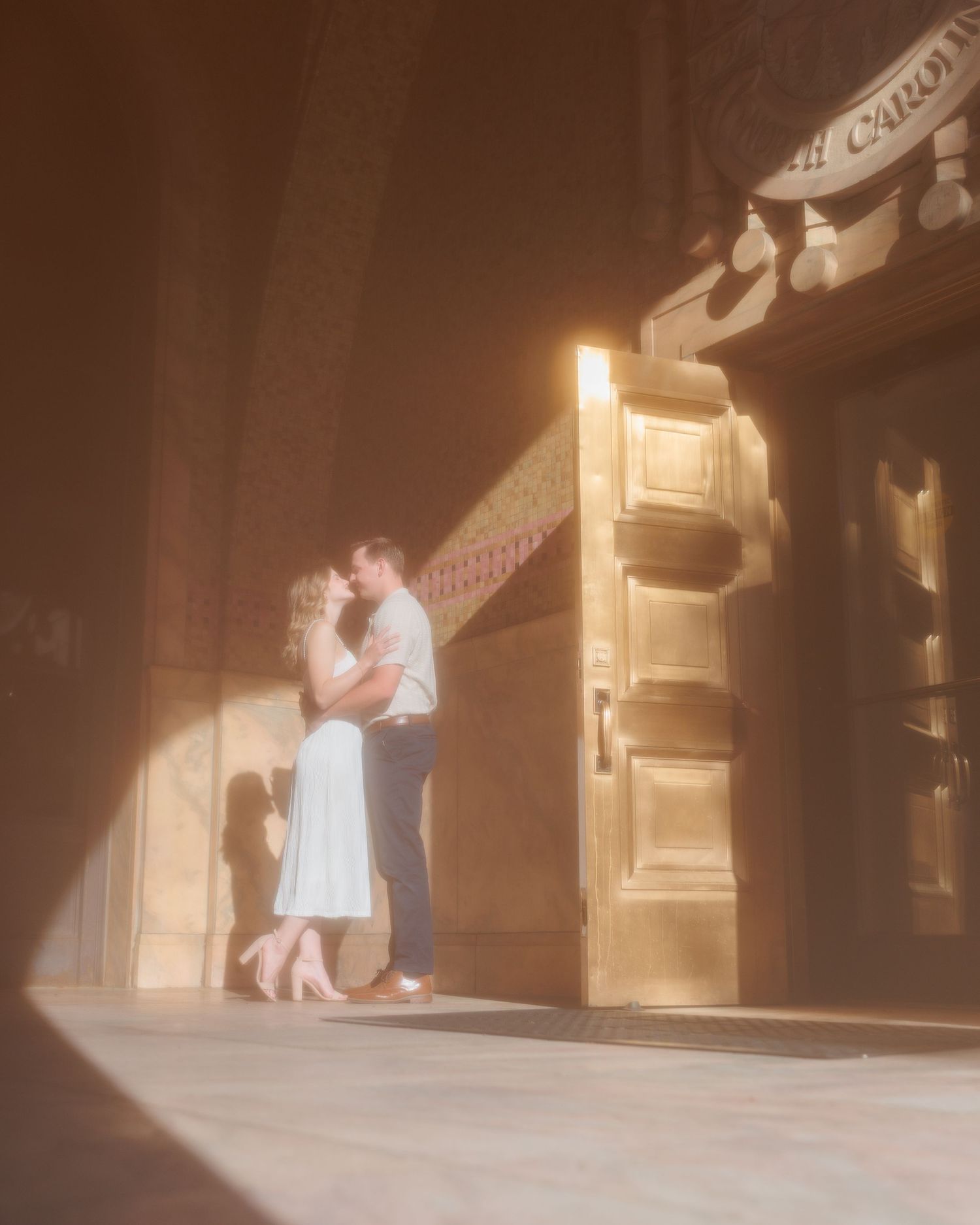 A couple embraces in a softly lit doorway, creating a romantic vintage-style scene with warm sepia tones.