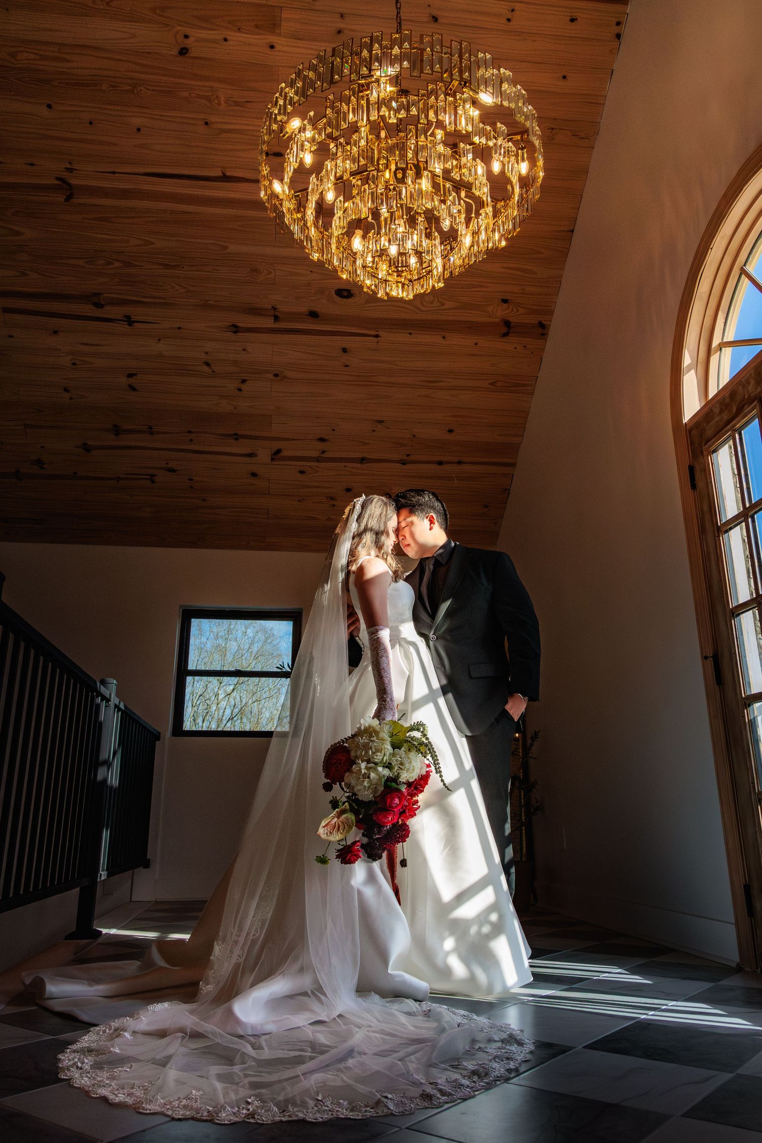 A stunning crystal chandelier illuminates a wedding scene with natural light streaming through windows.