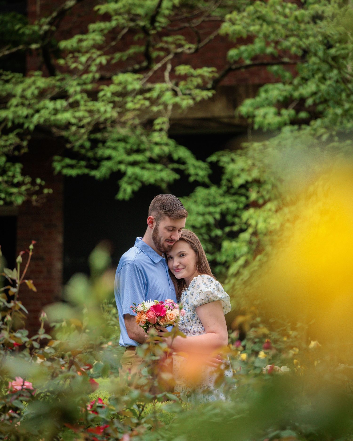 A couple shares an intimate moment among blooming flowers and lush greenery in a romantic garden setting.