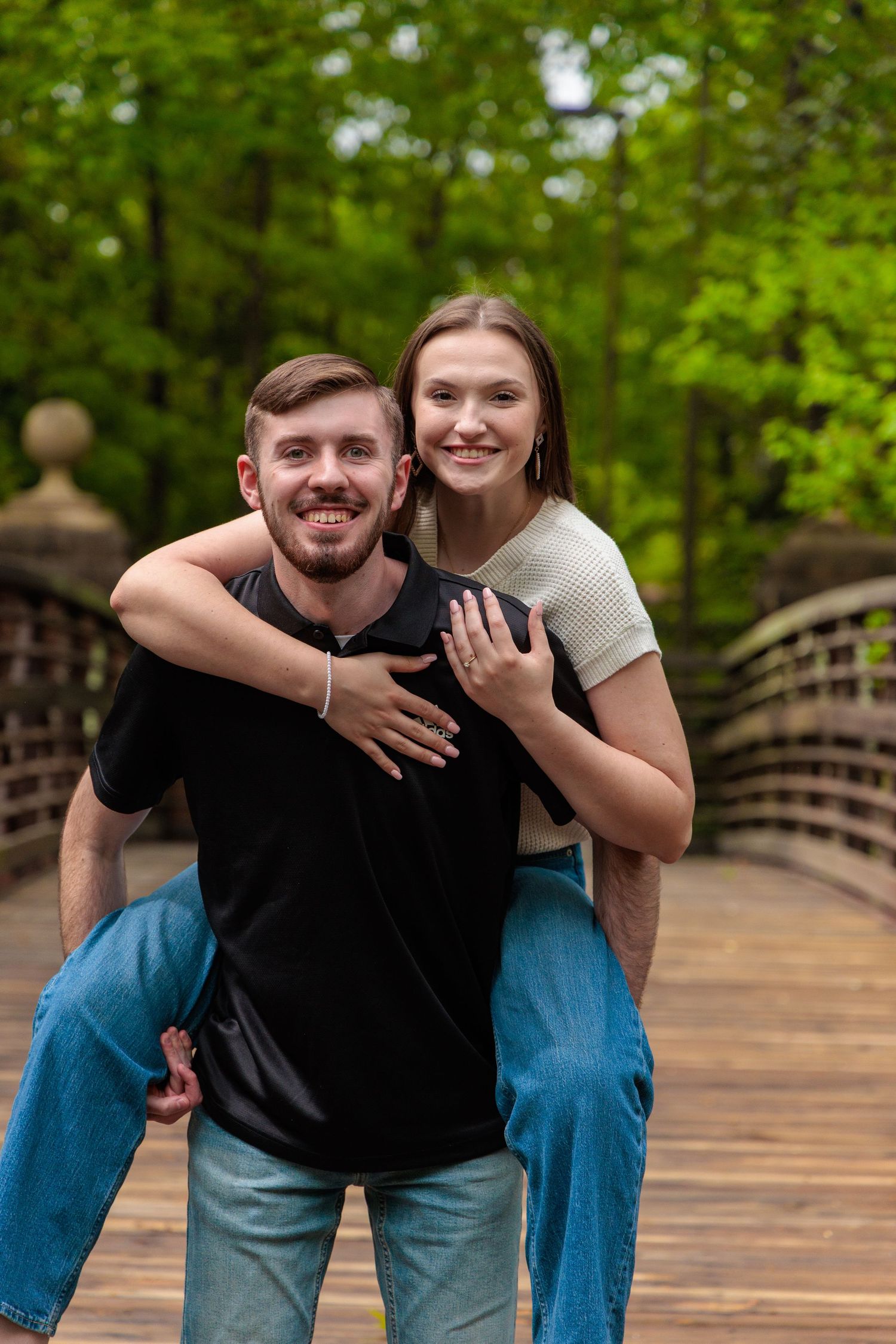 A couple shares a joyful moment on a wooden bridge surrounded by vibrant green trees.