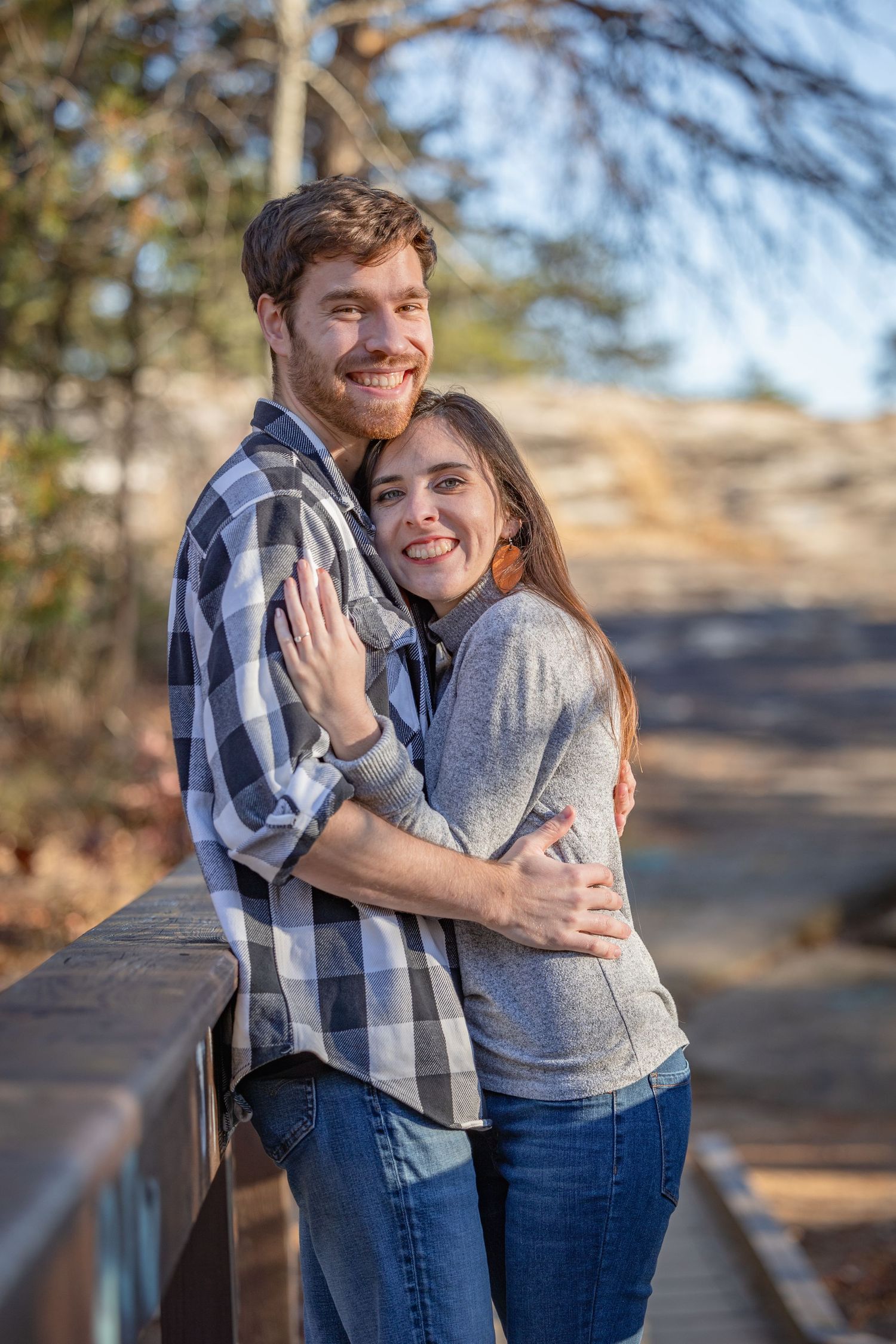 A couple embraces while standing on a wooden bridge in an outdoor setting.