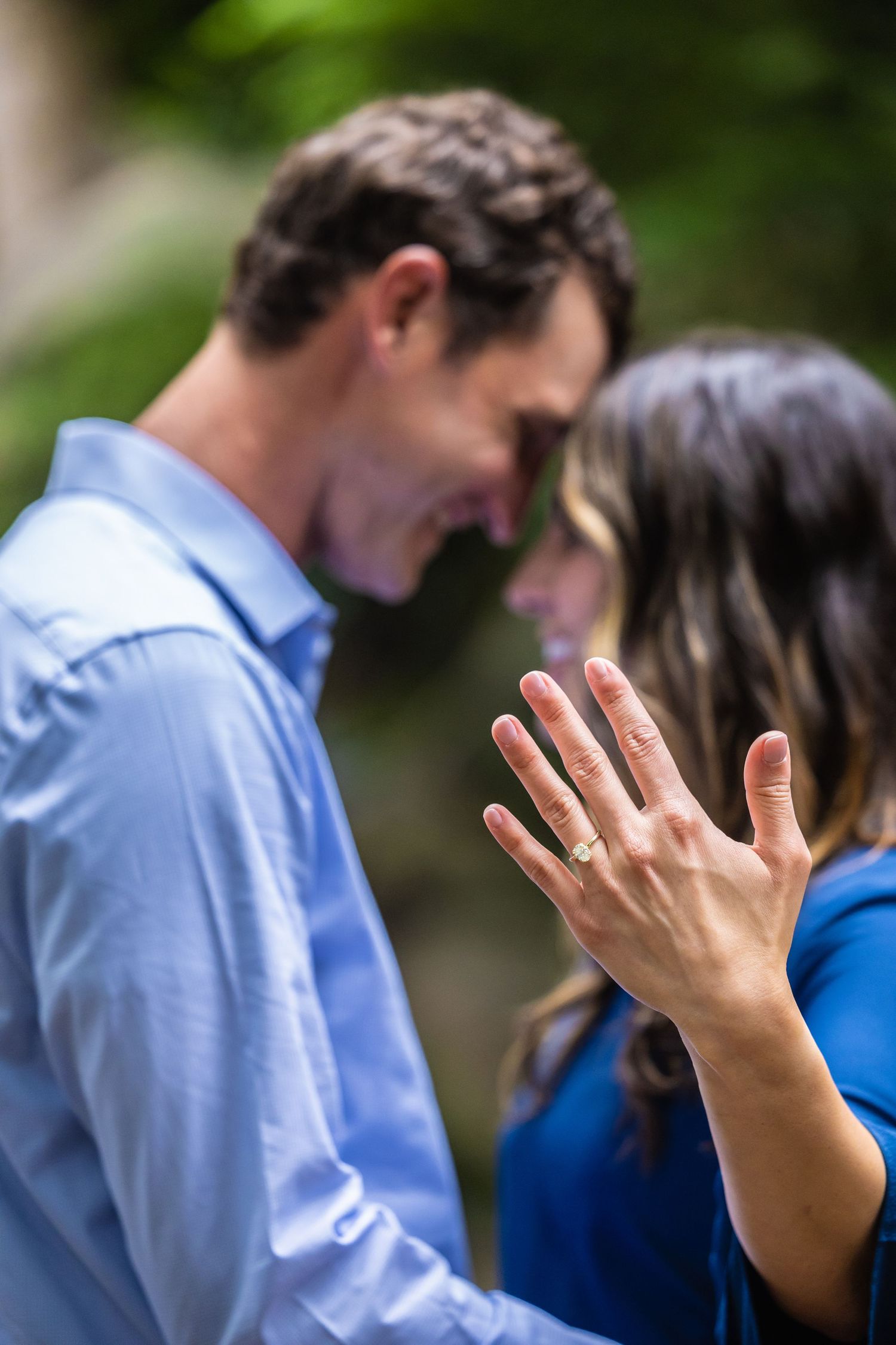 A couple sharing an intimate moment outdoors as someone shows off their engagement ring.