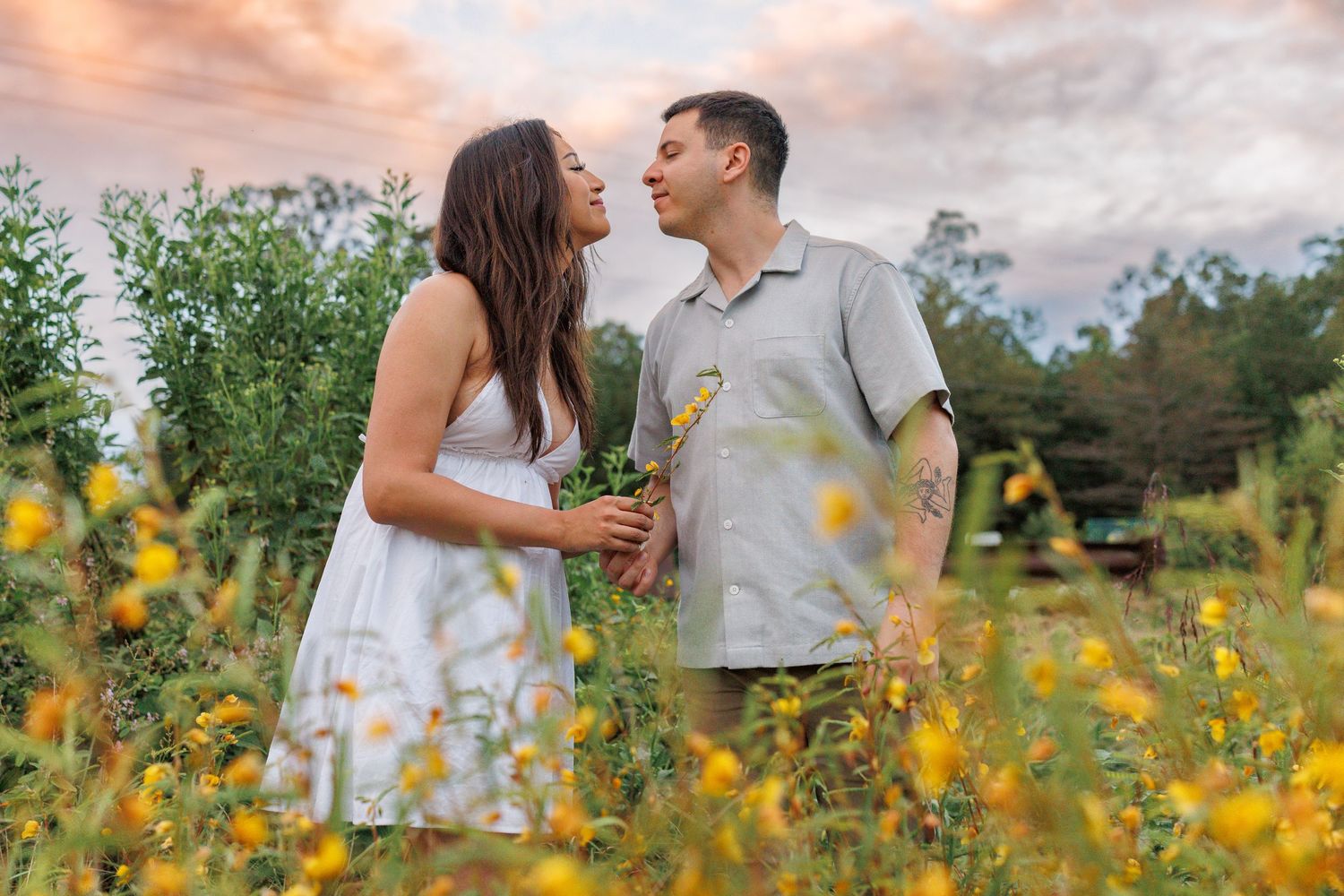 A couple embraces lovingly in a field of vibrant yellow wildflowers during a sunny summer afternoon.