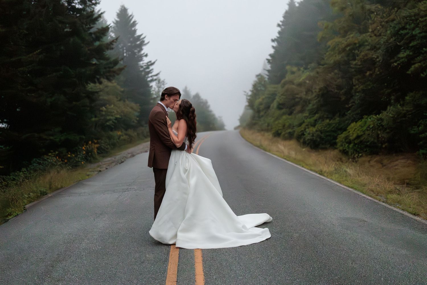 A graceful figure in a white dress twirls on a misty forest road creating an ethereal movement effect.