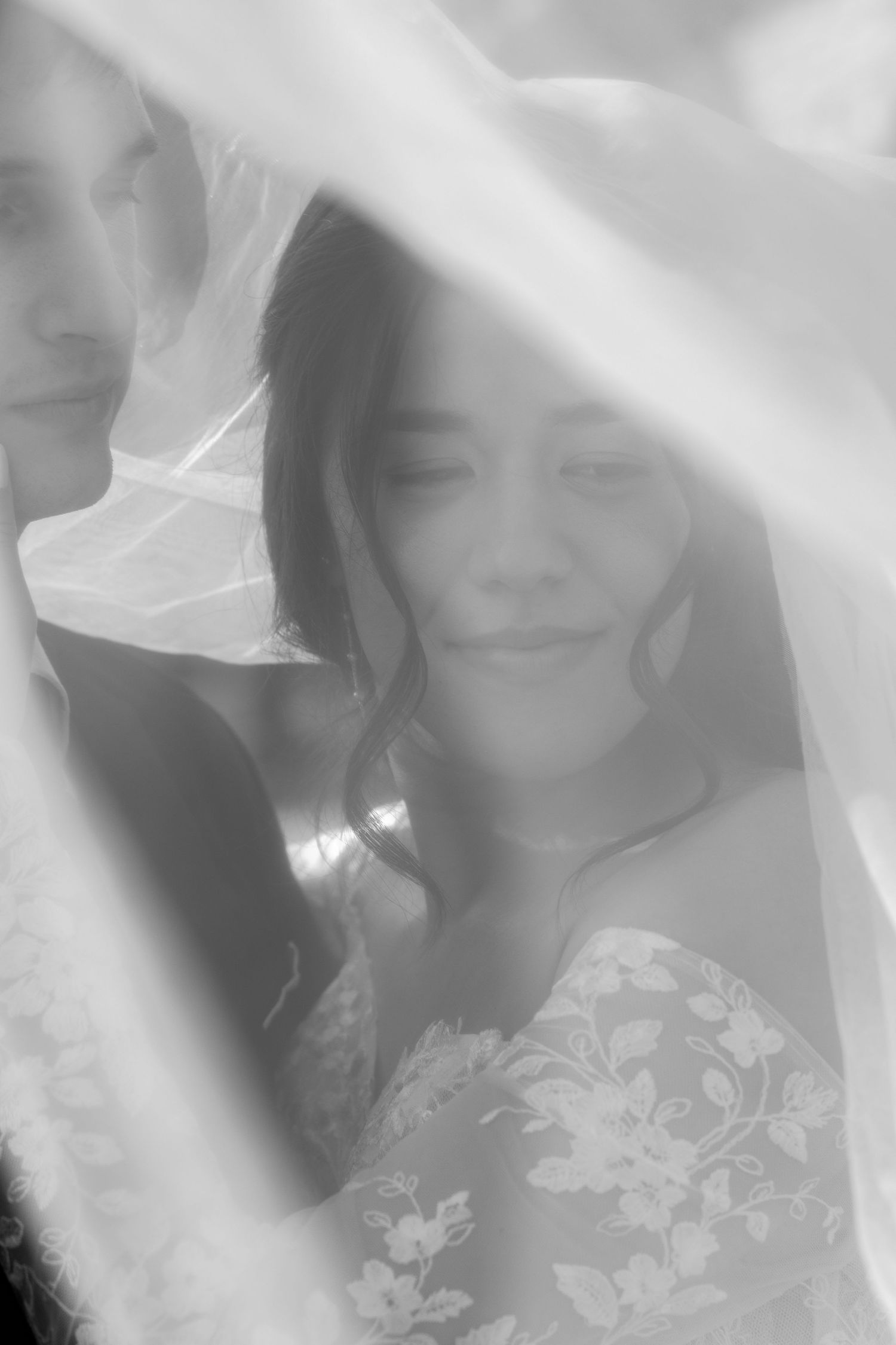 A soft black and white portrait of a bride under her veil with delicate lace details.