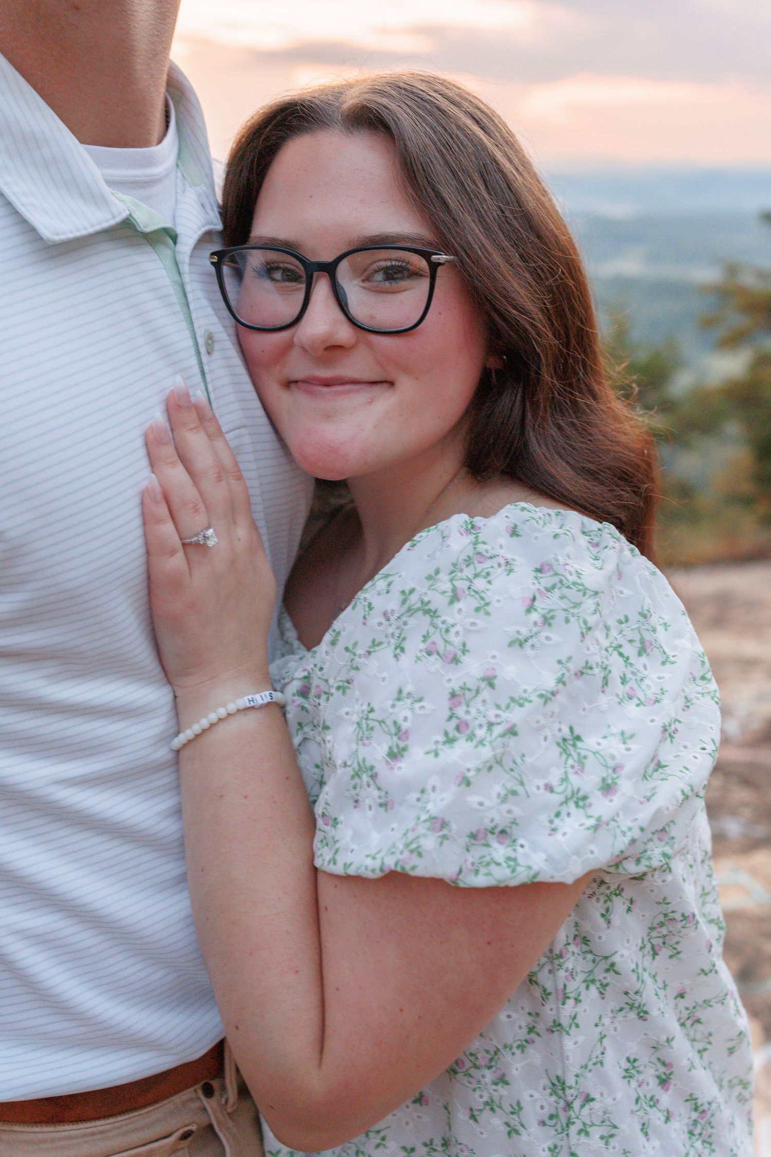 A couple embraces during an outdoor engagement photoshoot with mountains visible in the background.