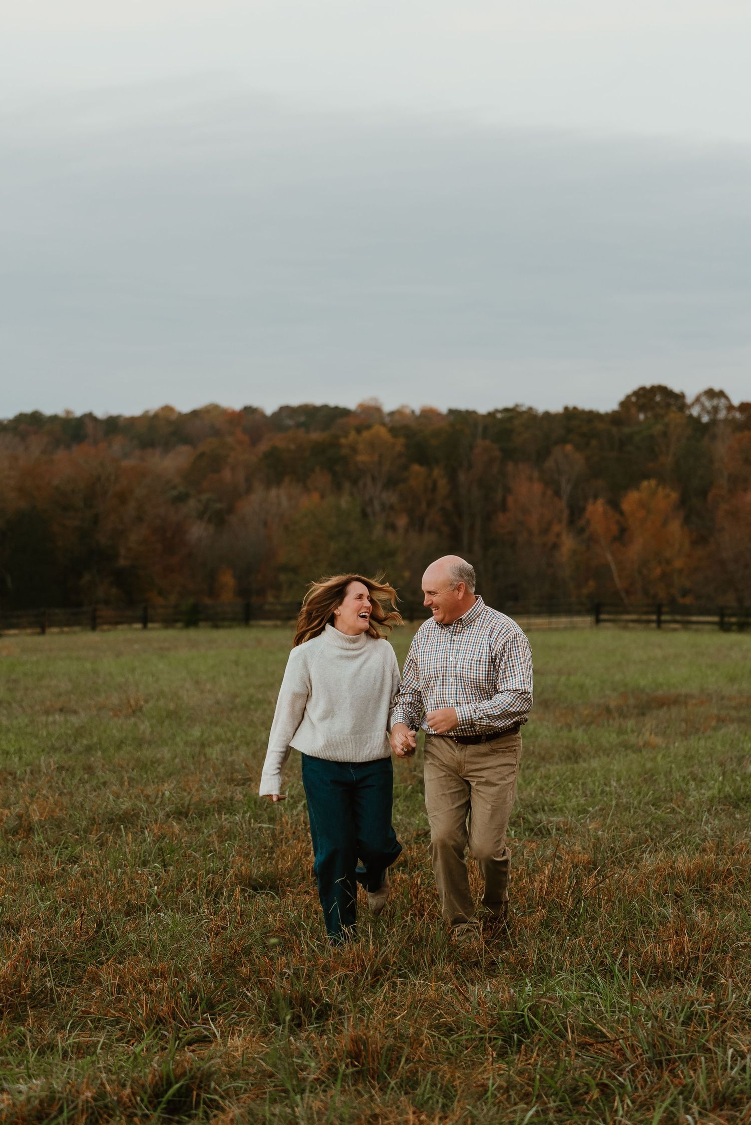 Joyful couple holding hands and laughing while running through an open fall field.