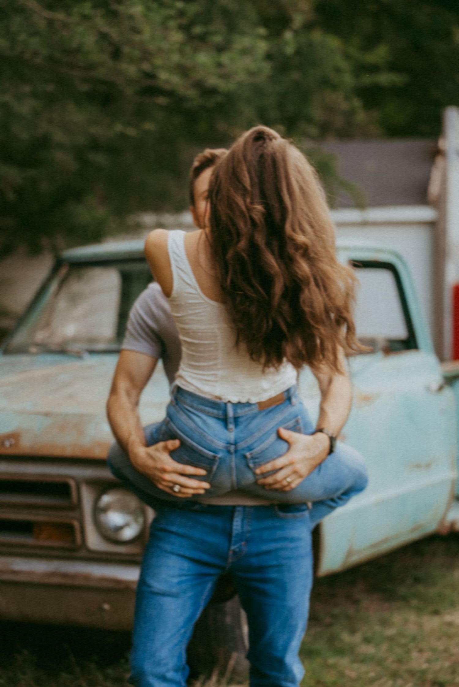 Man lifting woman in front of a vintage turquoise pickup truck during outdoor couples session.