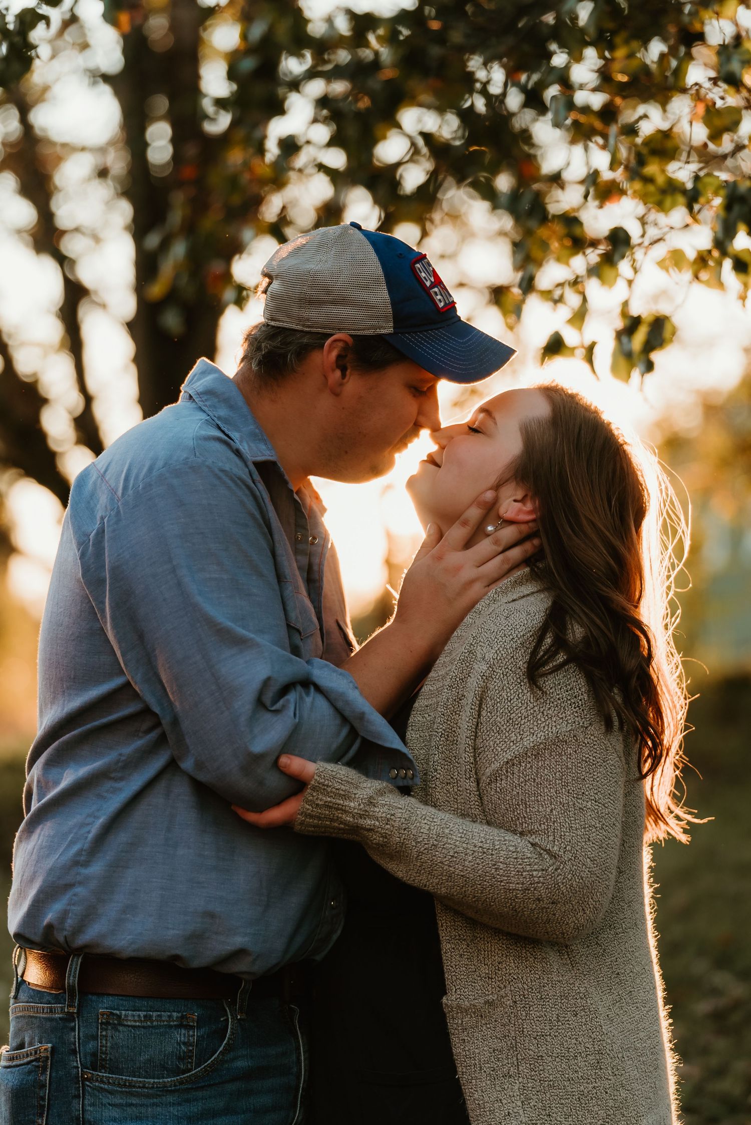 Couple sharing a romantic kiss at golden hour with warm sunlight behind them.
