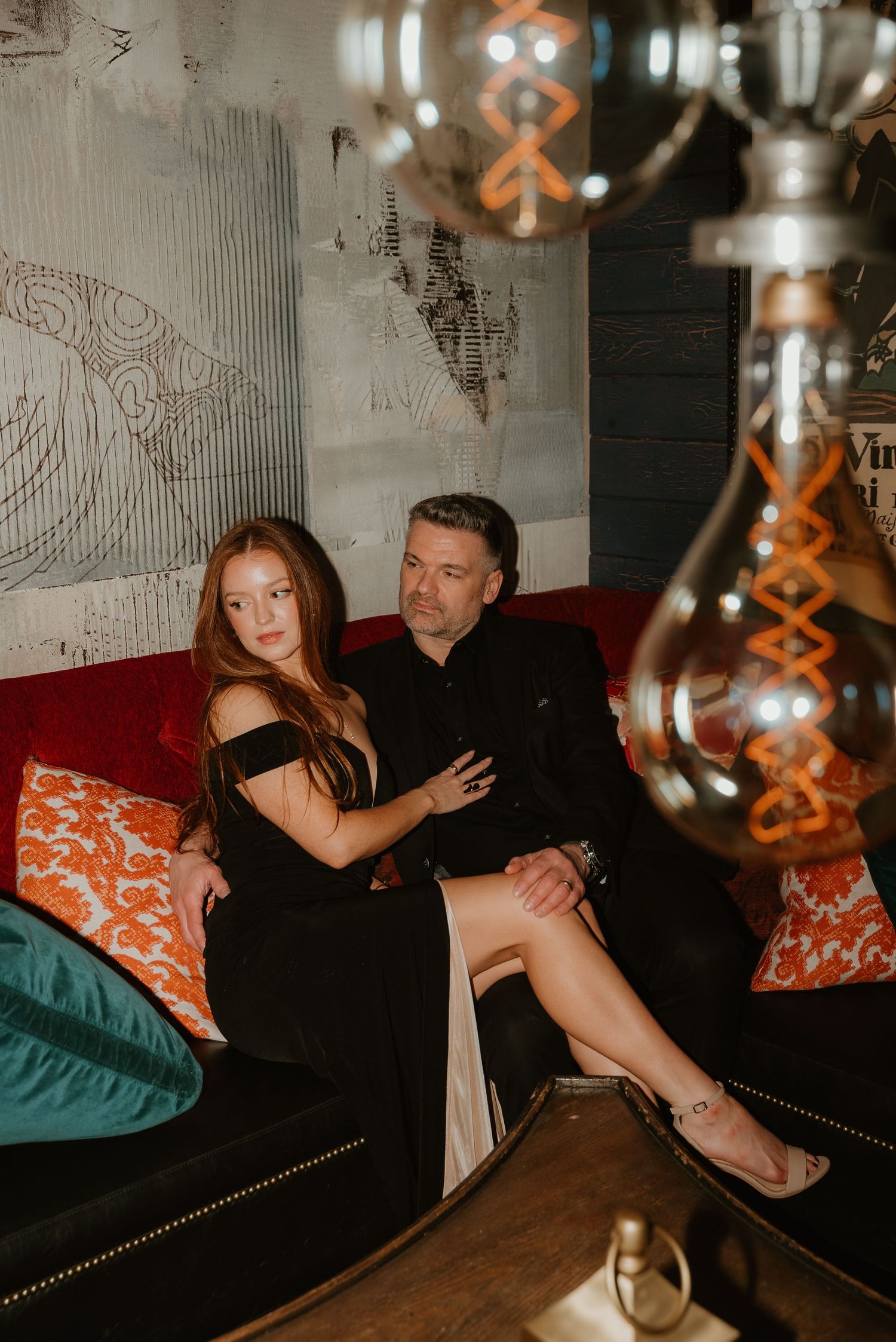 Couple sitting together on a red velvet couch in a stylish dimly lit lounge.