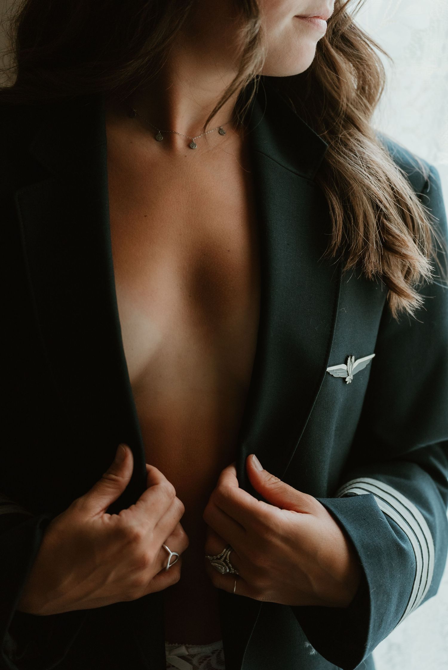 Woman opening dark jacket revealing bare chest with pilot wings pin.
