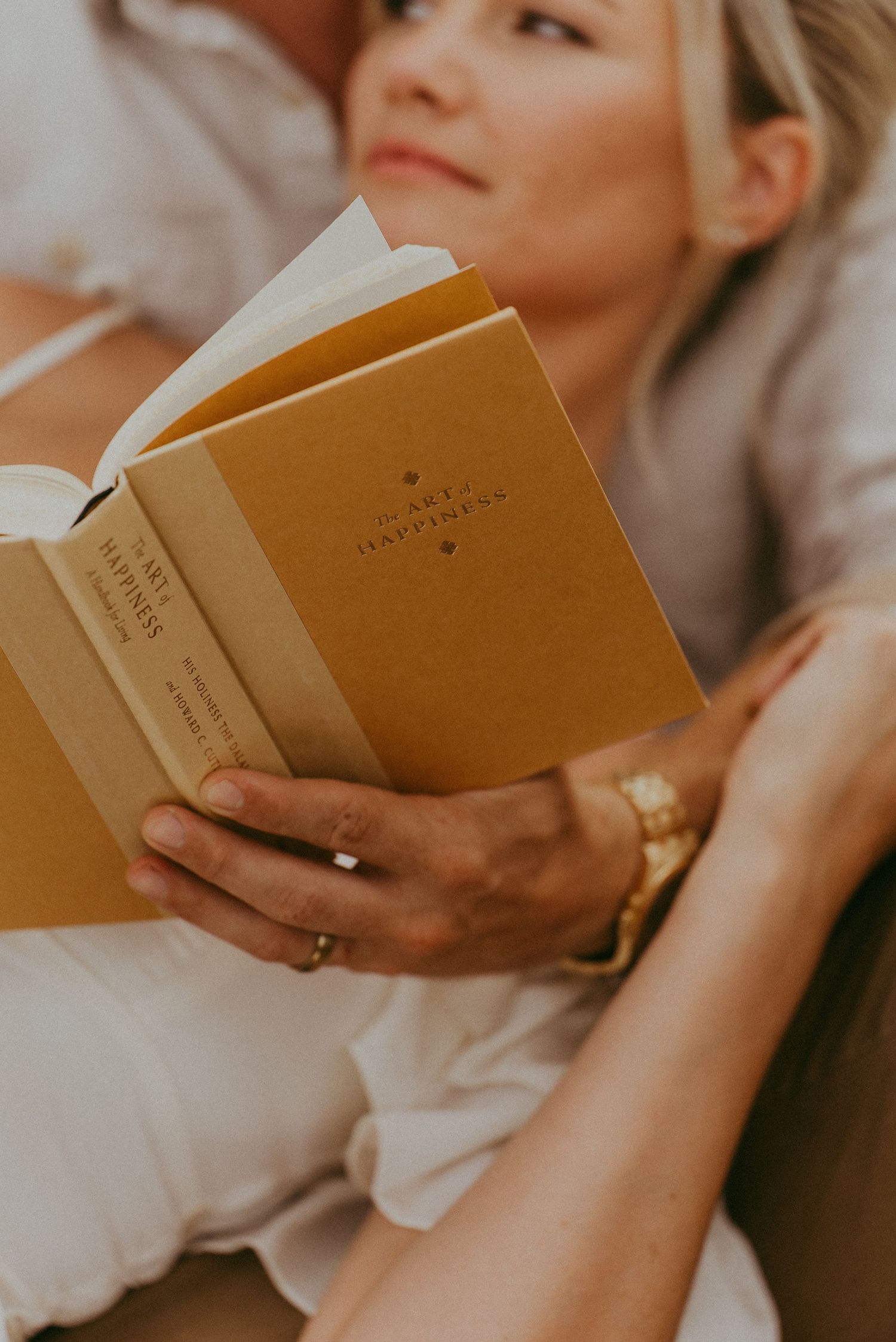 Close-up of a woman holding a yellow vintage book while relaxing in a mans arms outdoors.