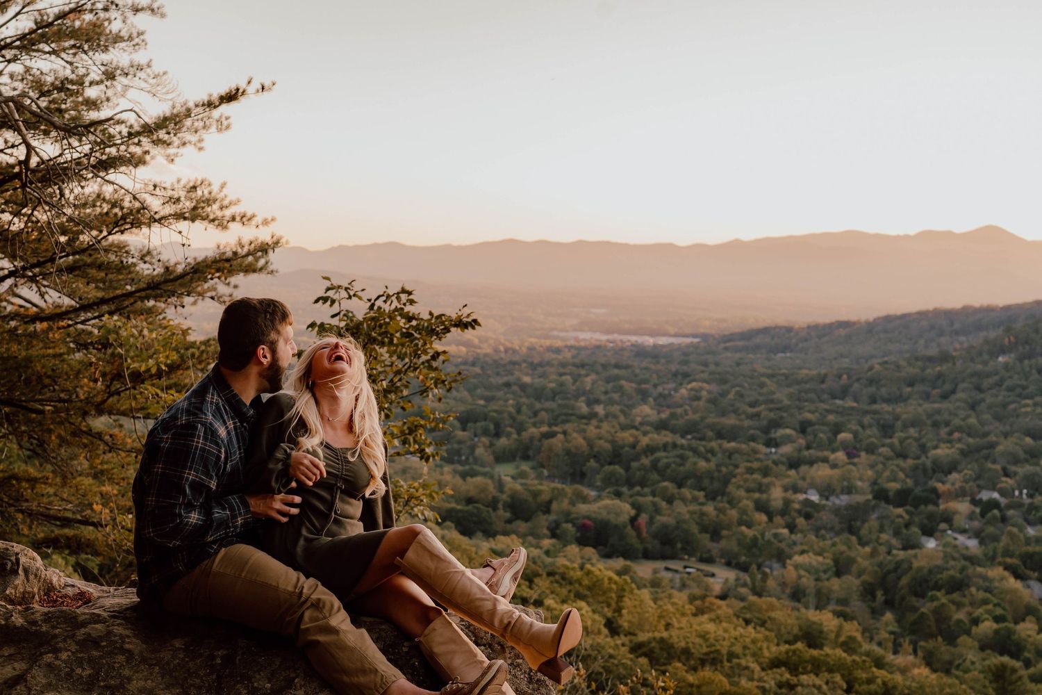 Couple sitting on a rocky overlook at sunset, enjoying a scenic mountain valley view together.