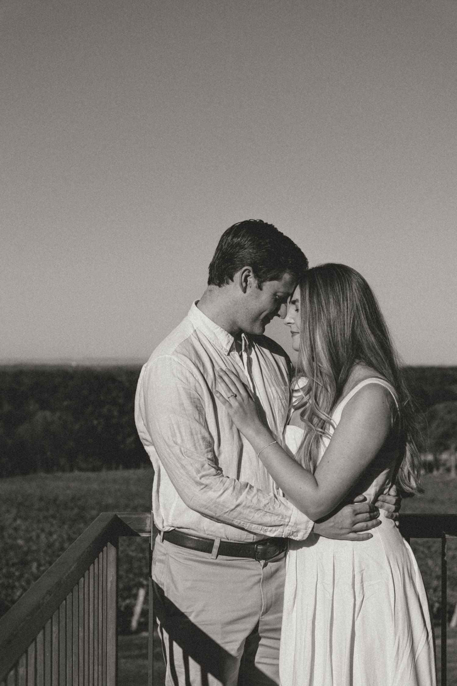 Black and white photo of couple embracing on a deck at golden hour.