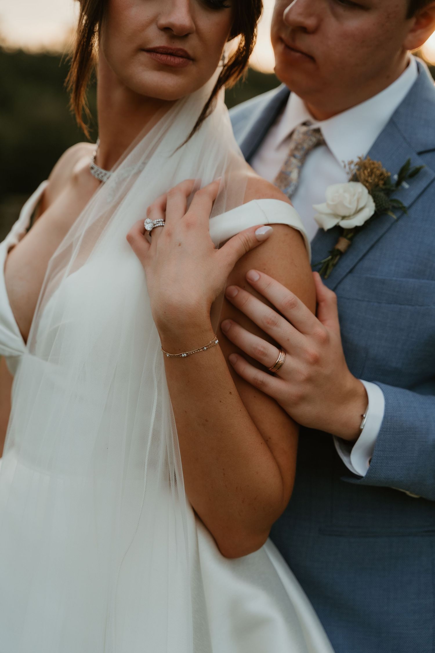 Close-up of bride and groom embracing, showcasing diamond engagement ring, wedding band, and delicate bracelet.