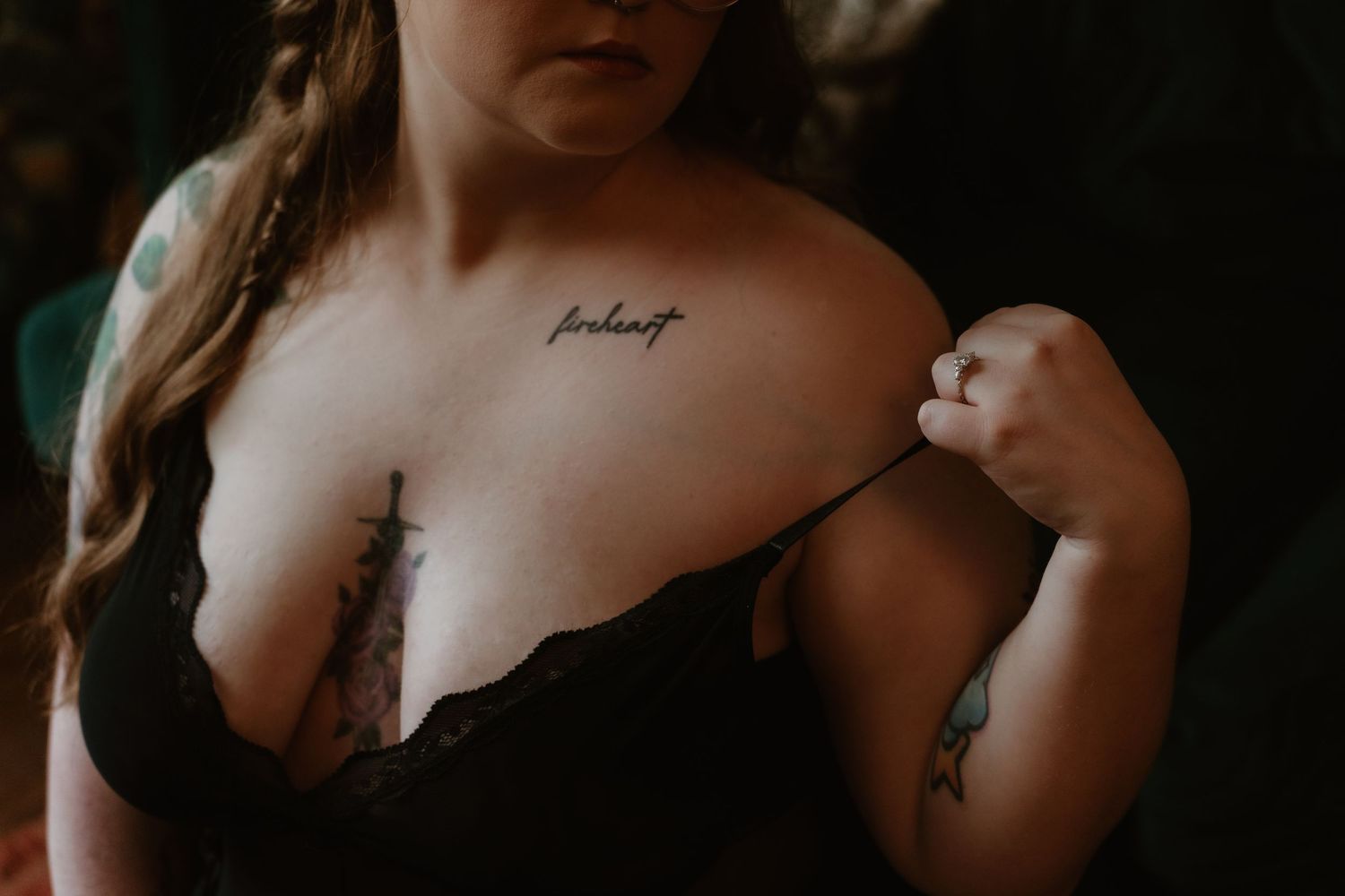Close-up of a woman in black lace bra with collarbone script tattoo and floral chest tattoos.