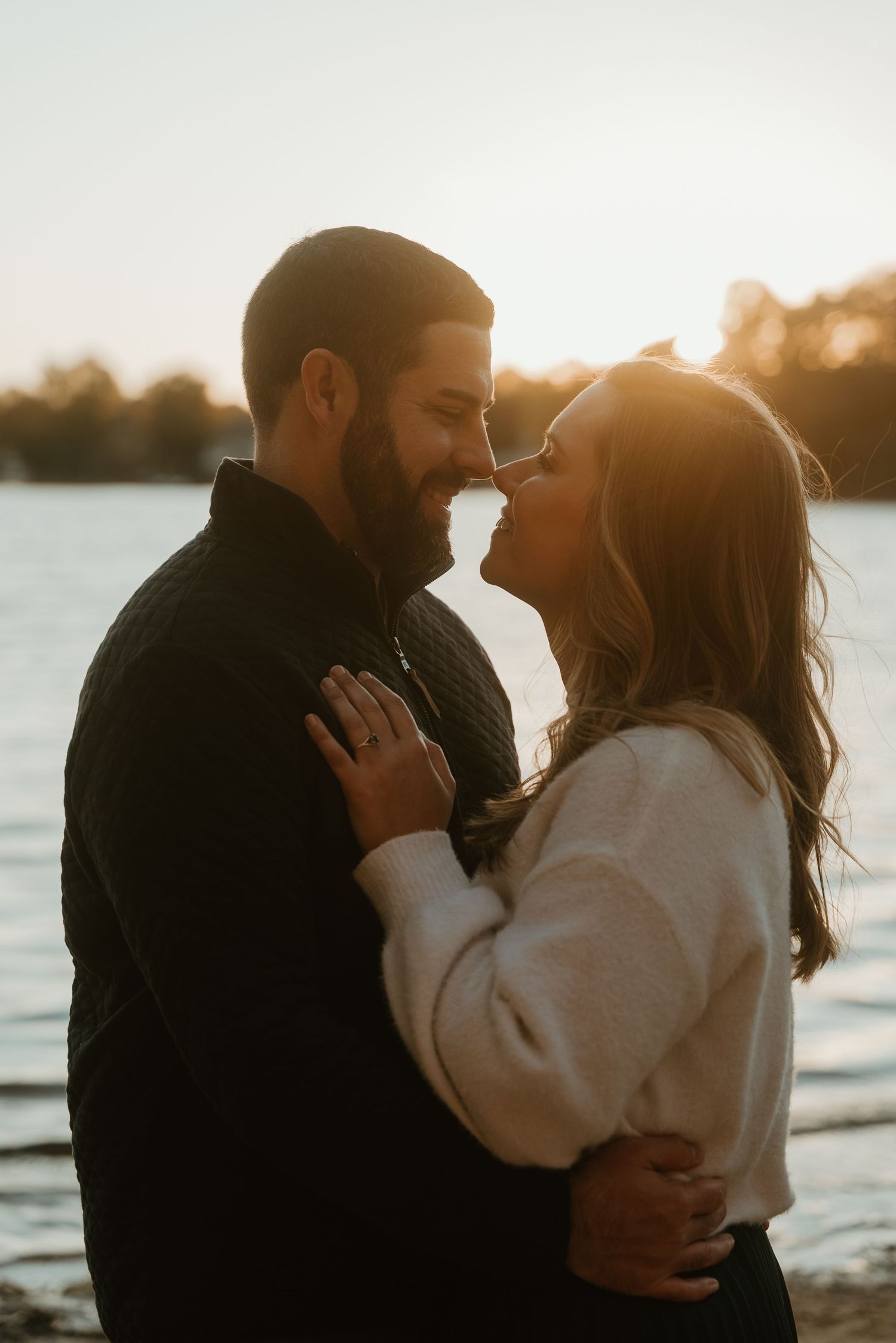Romantic couple embracing and smiling at each other in warm golden sunset light by lake.
