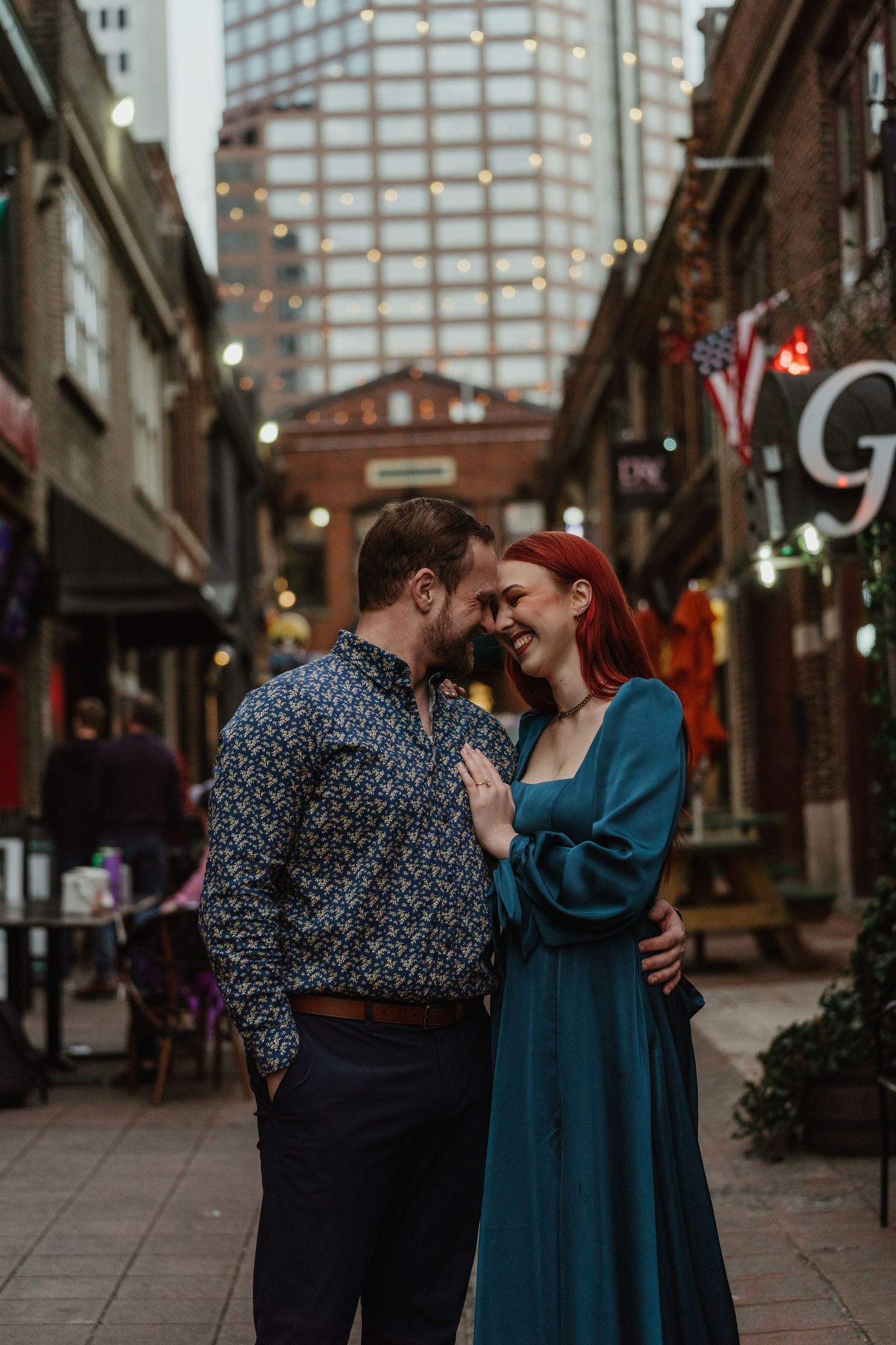 Smiling couple sharing a tender moment in a charming urban alley with string lights.