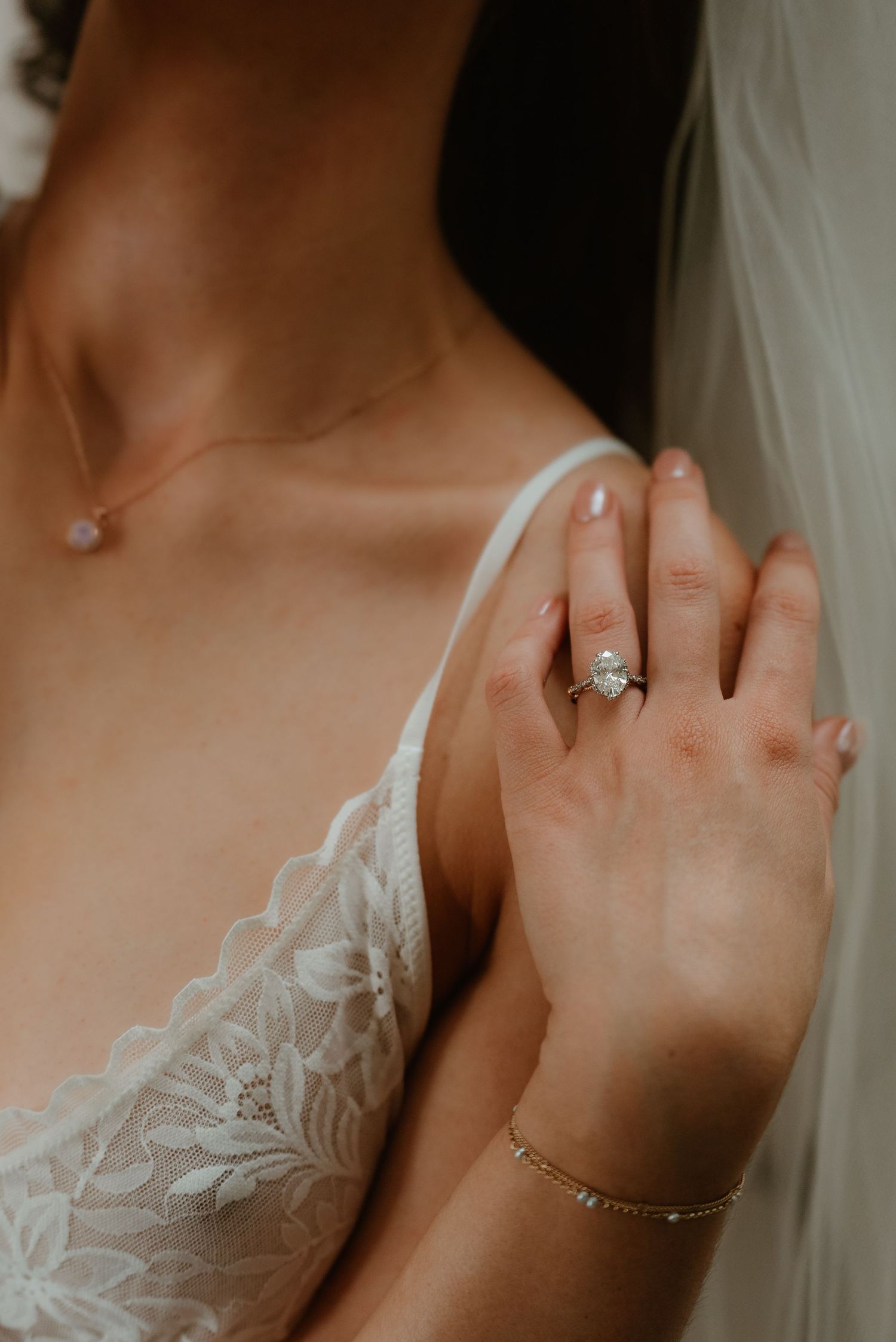 Close-up of bride wearing diamond engagement ring, lace gown, and delicate bracelet.