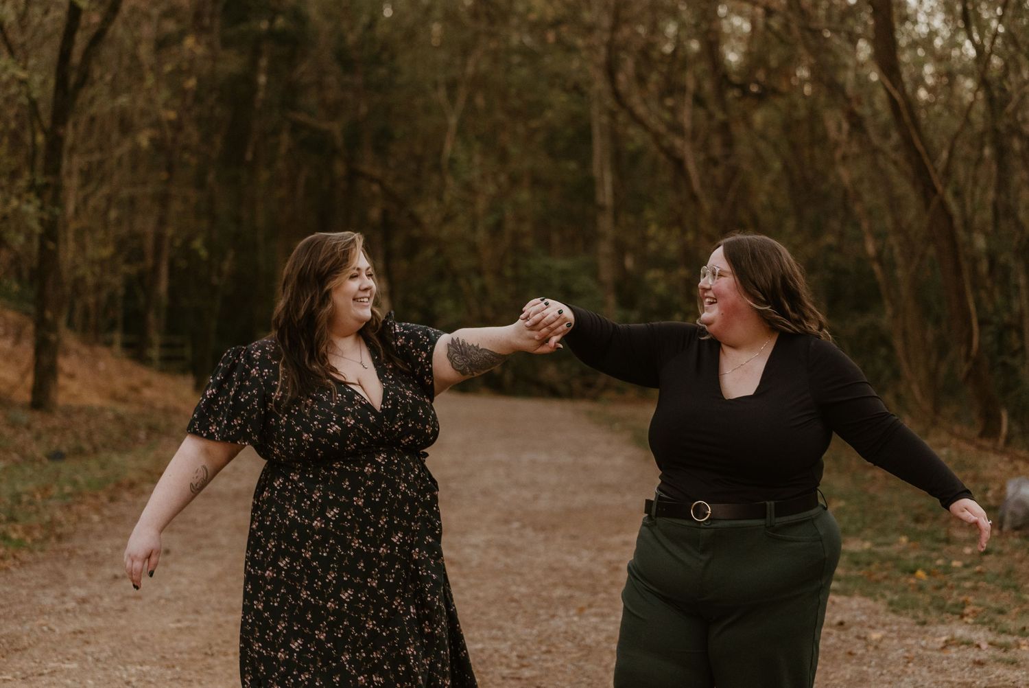 Two women laughing and dancing together on a woodland path in fall.