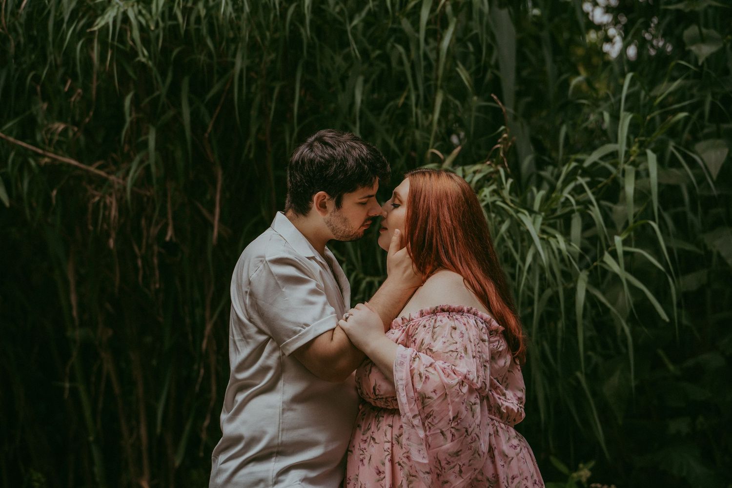 Young couple sharing a romantic almost-kiss moment surrounded by lush green bamboo foliage.