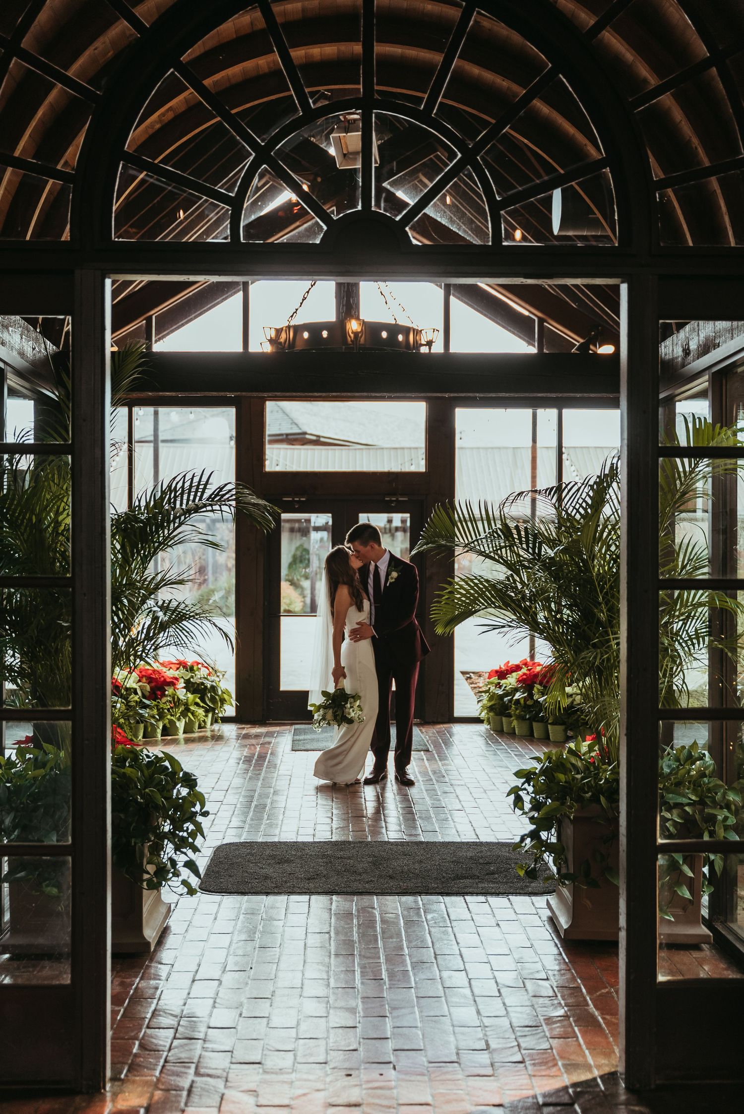 Bride and groom sharing intimate moment framed by elegant greenhouse archway entrance.