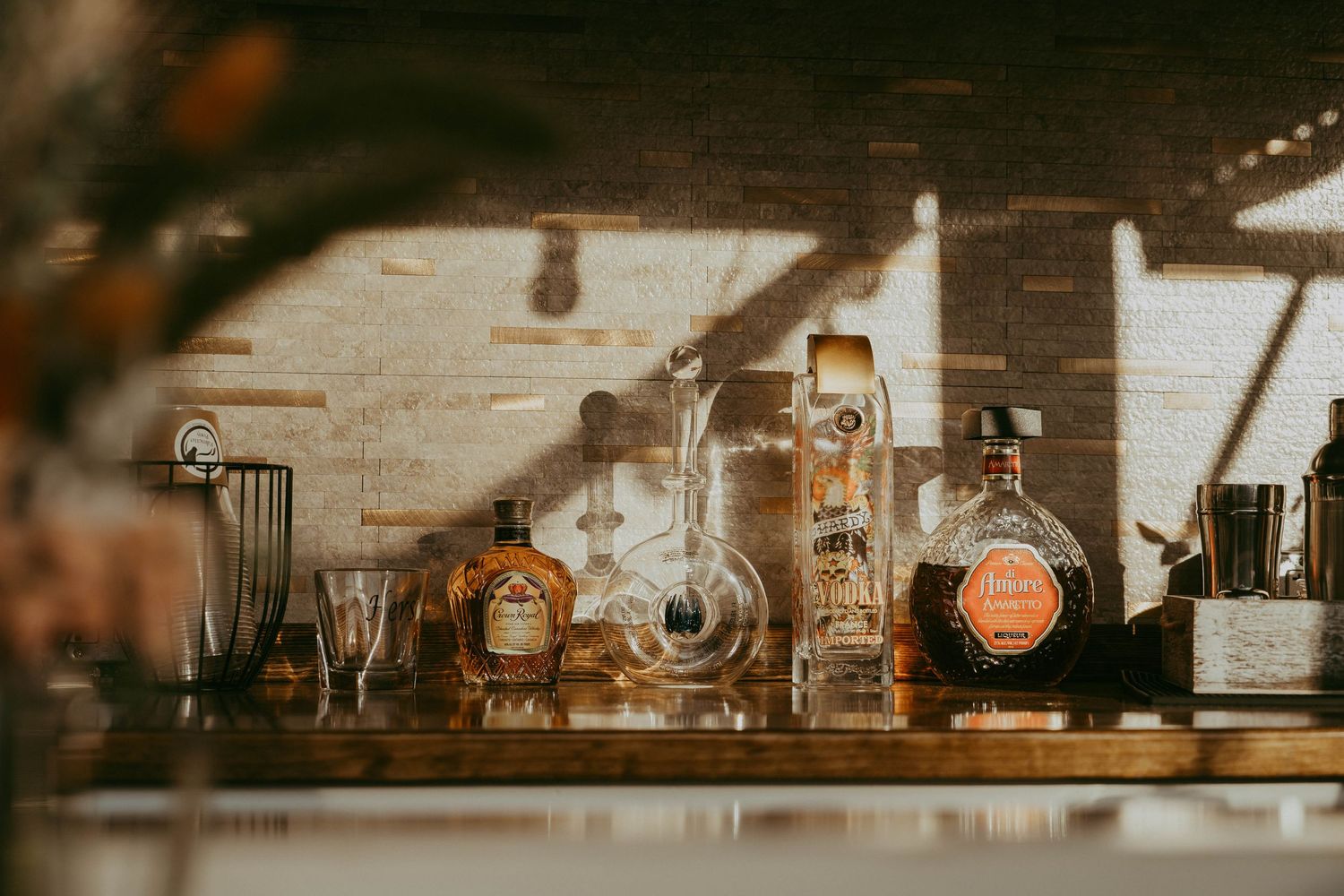 Elegant bar shelf display with whiskey bottles and glassware in warm sunlit setting.